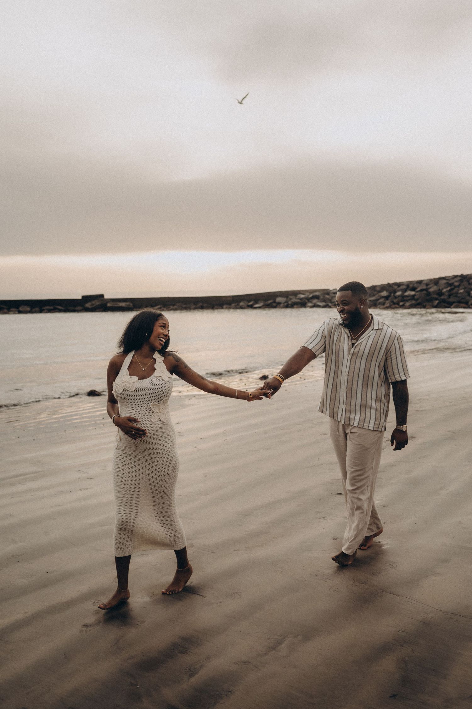 Pregnant woman leading partner holding hands along ocean at sunset, Playa Fañabé