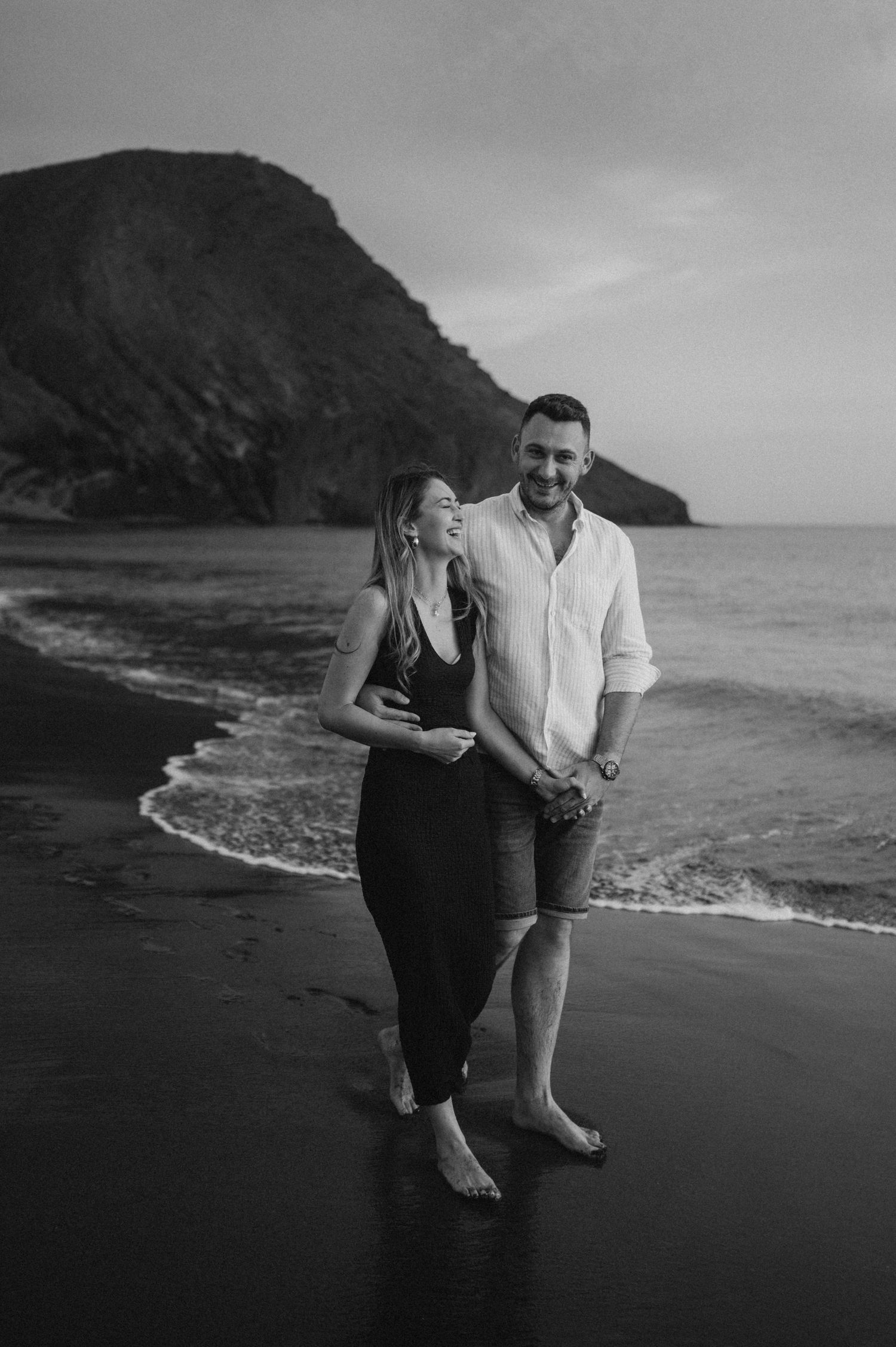 Romantic couple strolling on Playa de La Tejita beach at sunset with Montaña Roja, Tenerife