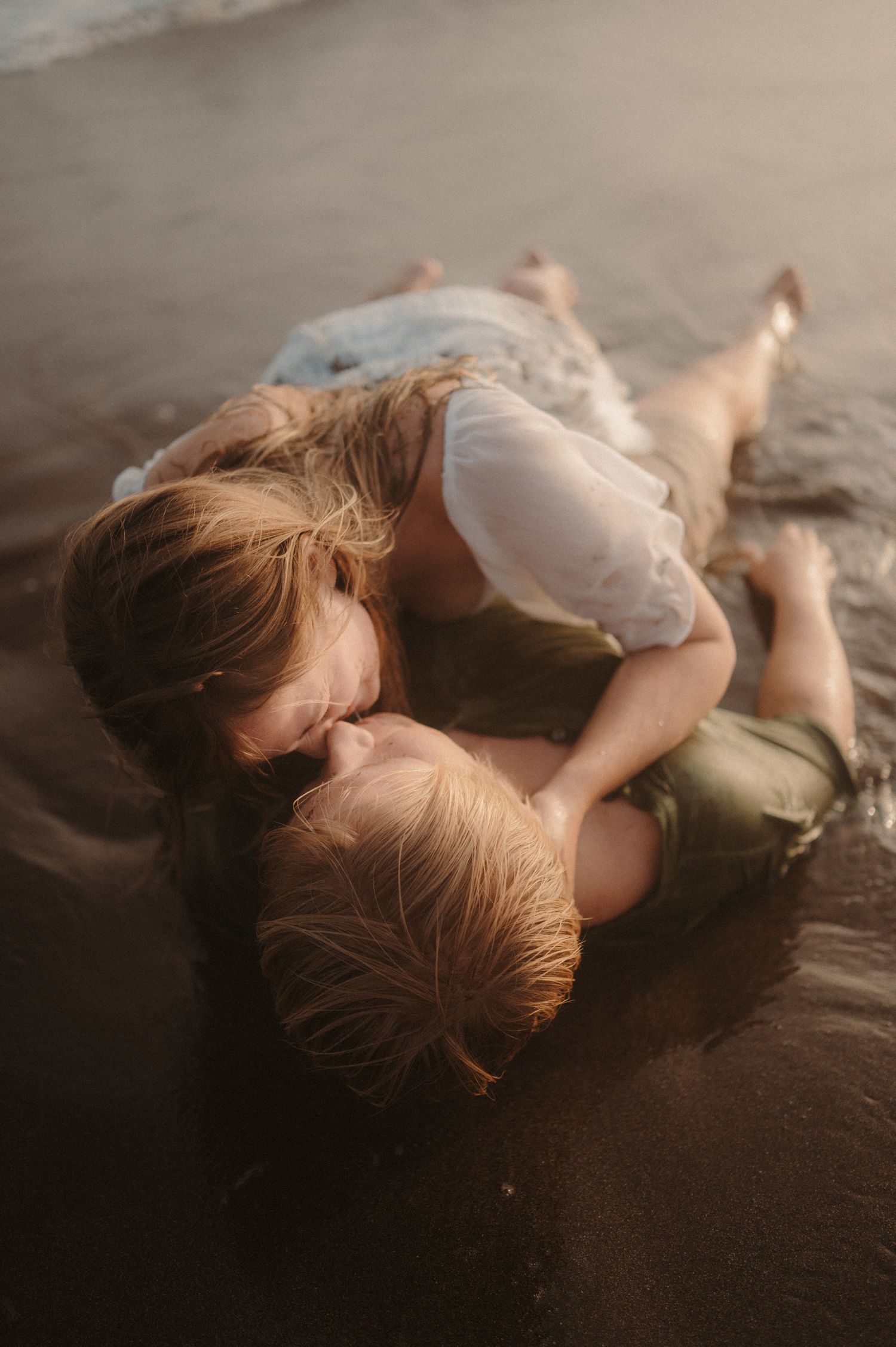 Couple embracing while lying in the ocean waves at Playa Tejita with sunset in the background, Tenerife couples photoshoot
