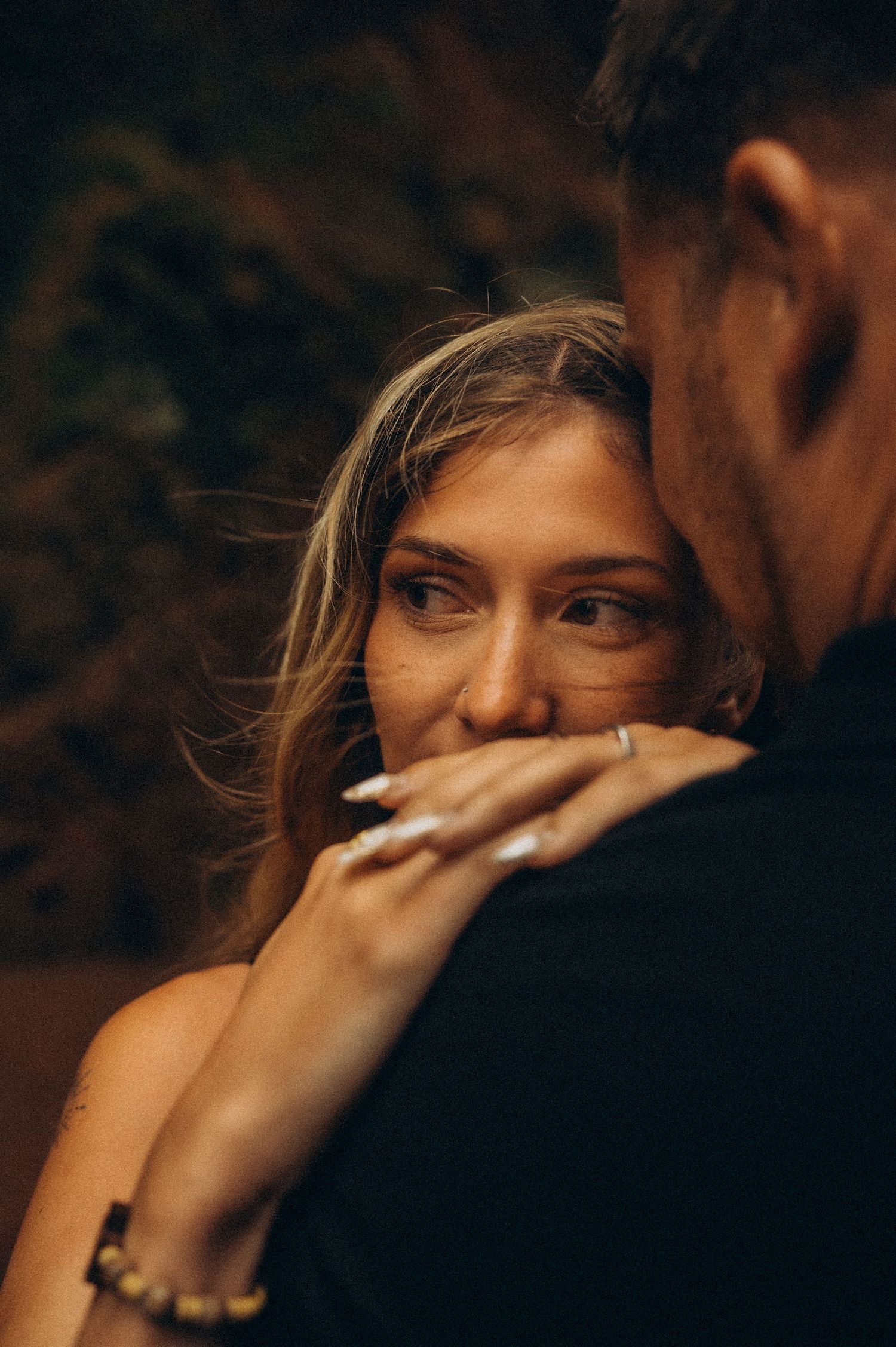 A woman with blonde hair smiles warmly while embracing a man, her hand resting gently on his chest.