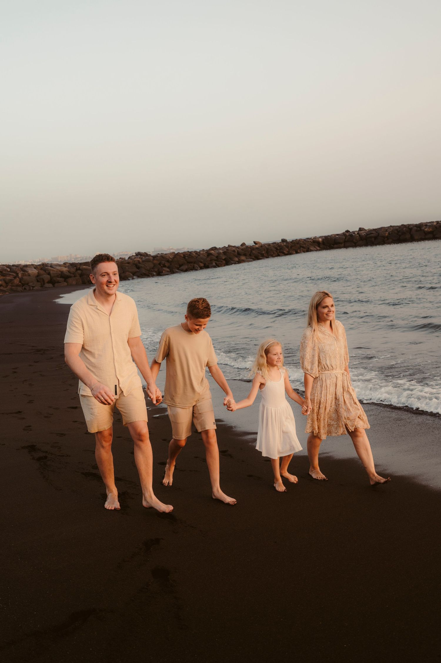 Family walking along black volcanic sand beach at sunset, Tenerife