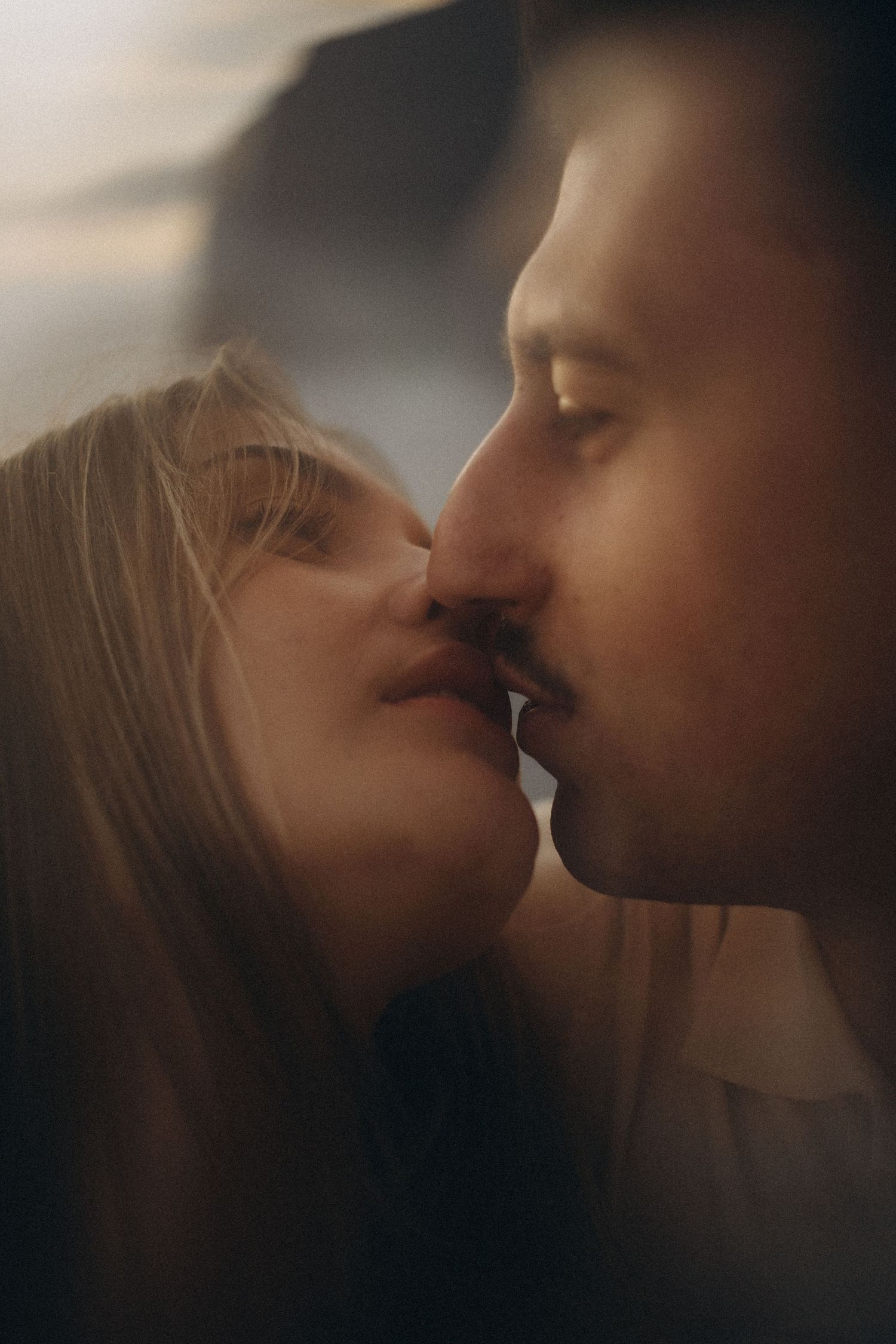 A romantic close-up of a couple about to kiss, bathed in warm golden light with a blurred outdoor backdrop.