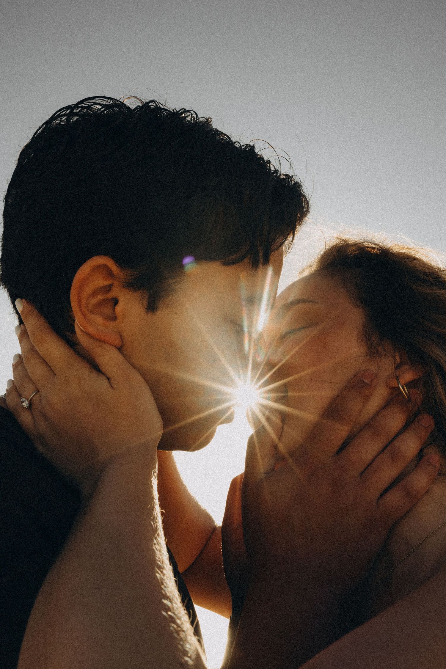 Couple sharing a romantic kiss with a stunning sunburst lens flare between them against a clear sky.