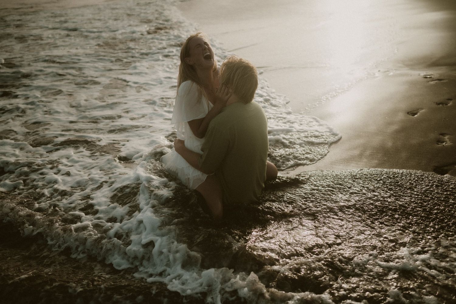 Couple lying in each other’s arms in the ocean at Playa Tejita during sunset, Tenerife couples photoshoot with waves in the background