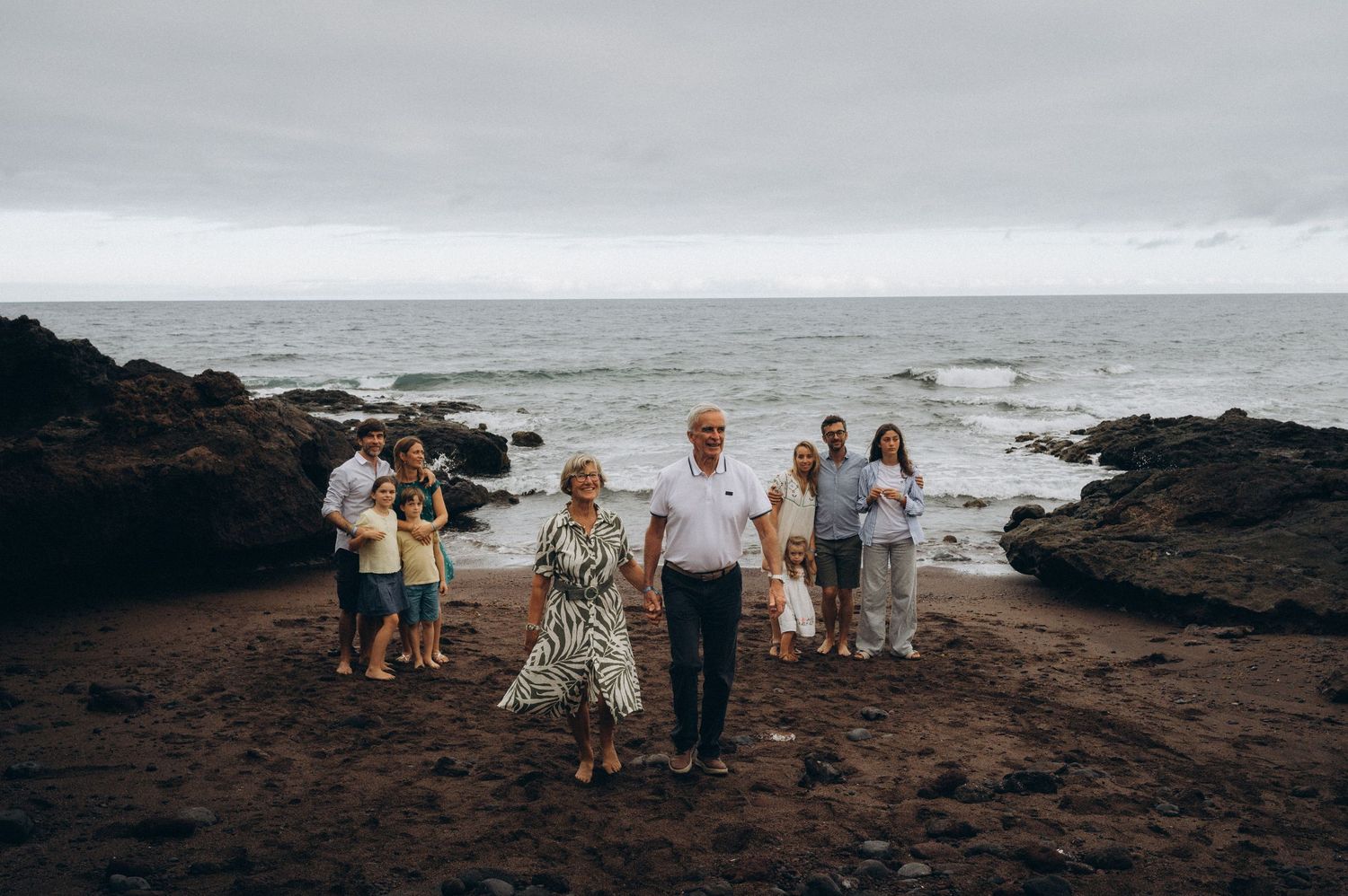 Families on black beach with dads on sides and grandparents approaching camera at Los Refugios, Tenerife