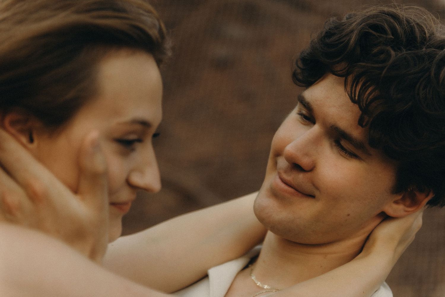 Romantic couple sharing an intimate moment, young man smiling tenderly at woman while she gazes up at him outdoors.