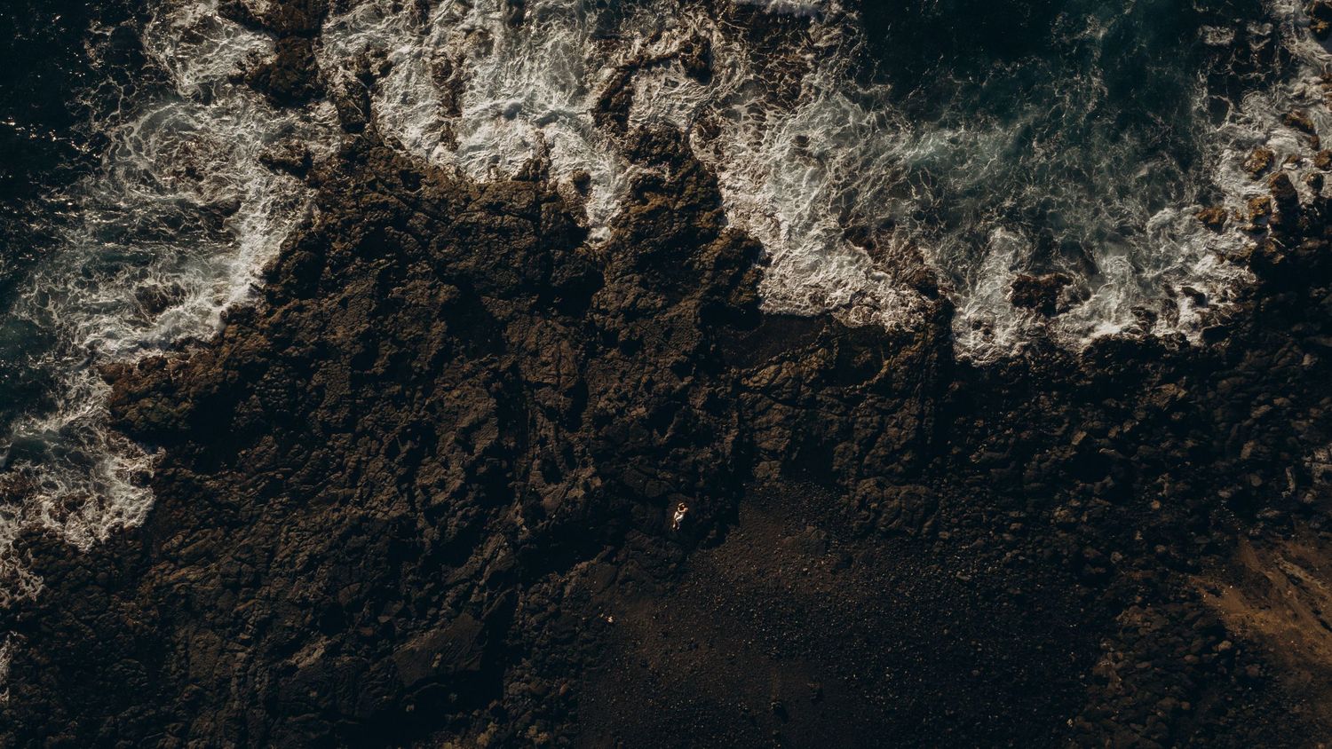 Dramatic aerial drone view of rugged mountain cliffs and rocky coastline along a misty shoreline in Tenerife.
