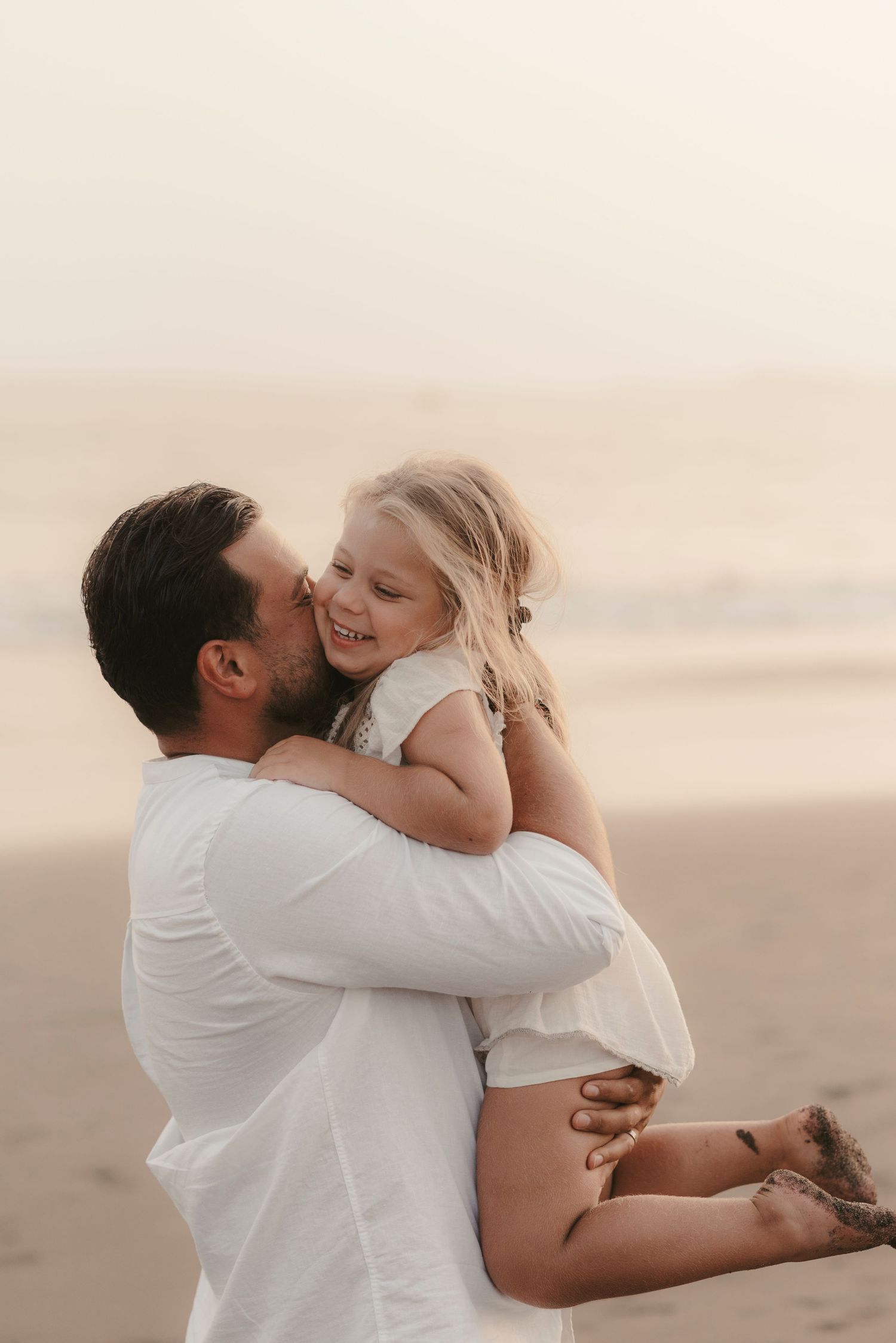 Loving father holding his daughter up and planting a gentle kiss on her cheek at Playa La Tejita