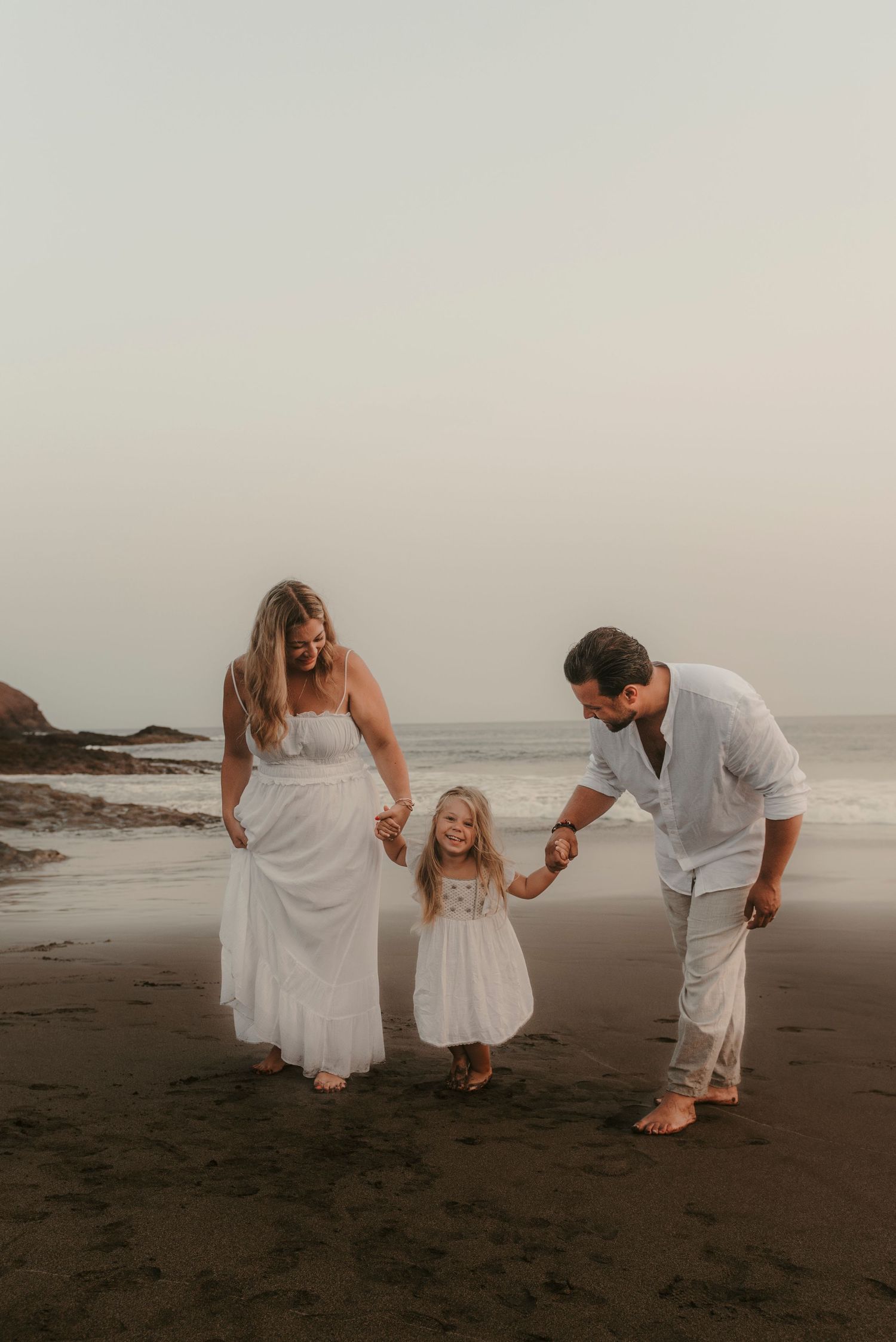 Tender scene of daughter between her parents, holding hands and looking at her father at Playa La Tejita, natural family photography