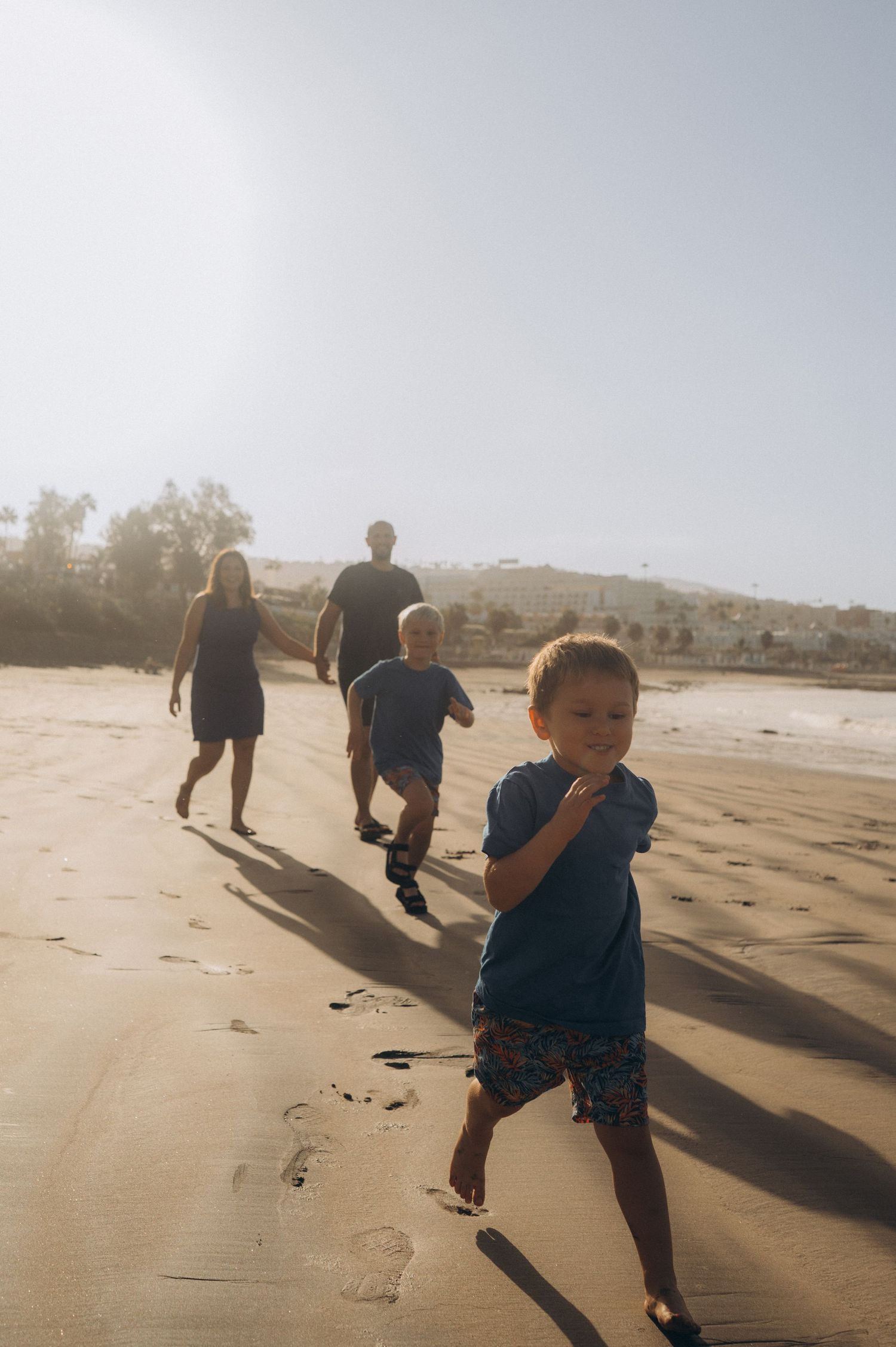 Parents walking on golden sand as their children run ahead with morning sun rays at Playa Fañabé, storytelling family photography