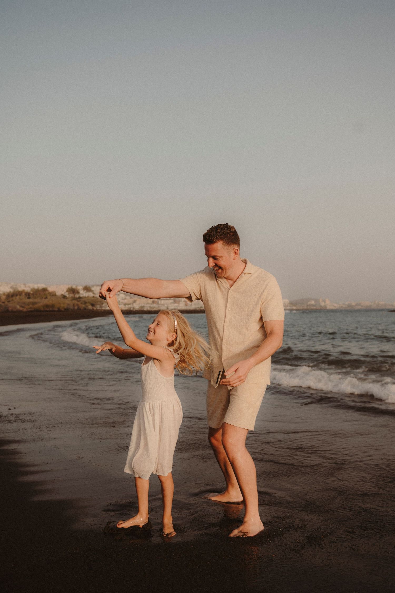 Father dancing with young daughter on black sand beach, Playa del Duque