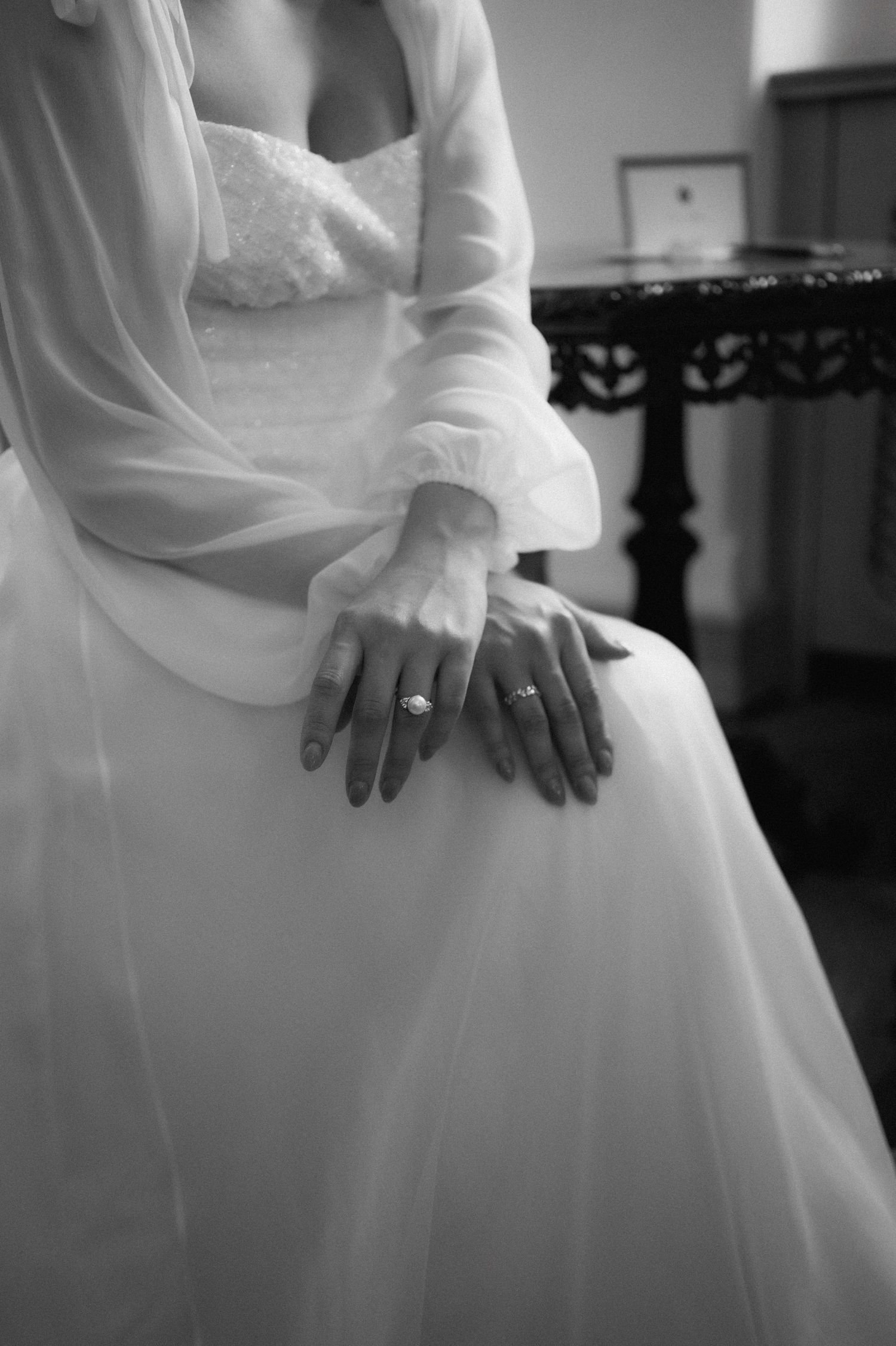 Elegant monochrome detail of the bride sitting with her hands folded over her lap in a refined bridal portrait.