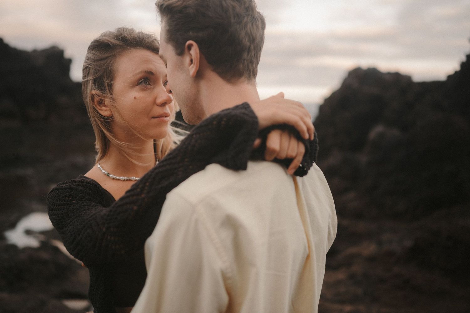 Close-up of a young romantic couple gazing into each other’s eyes with cliffs and ocean in the background, Tenerife