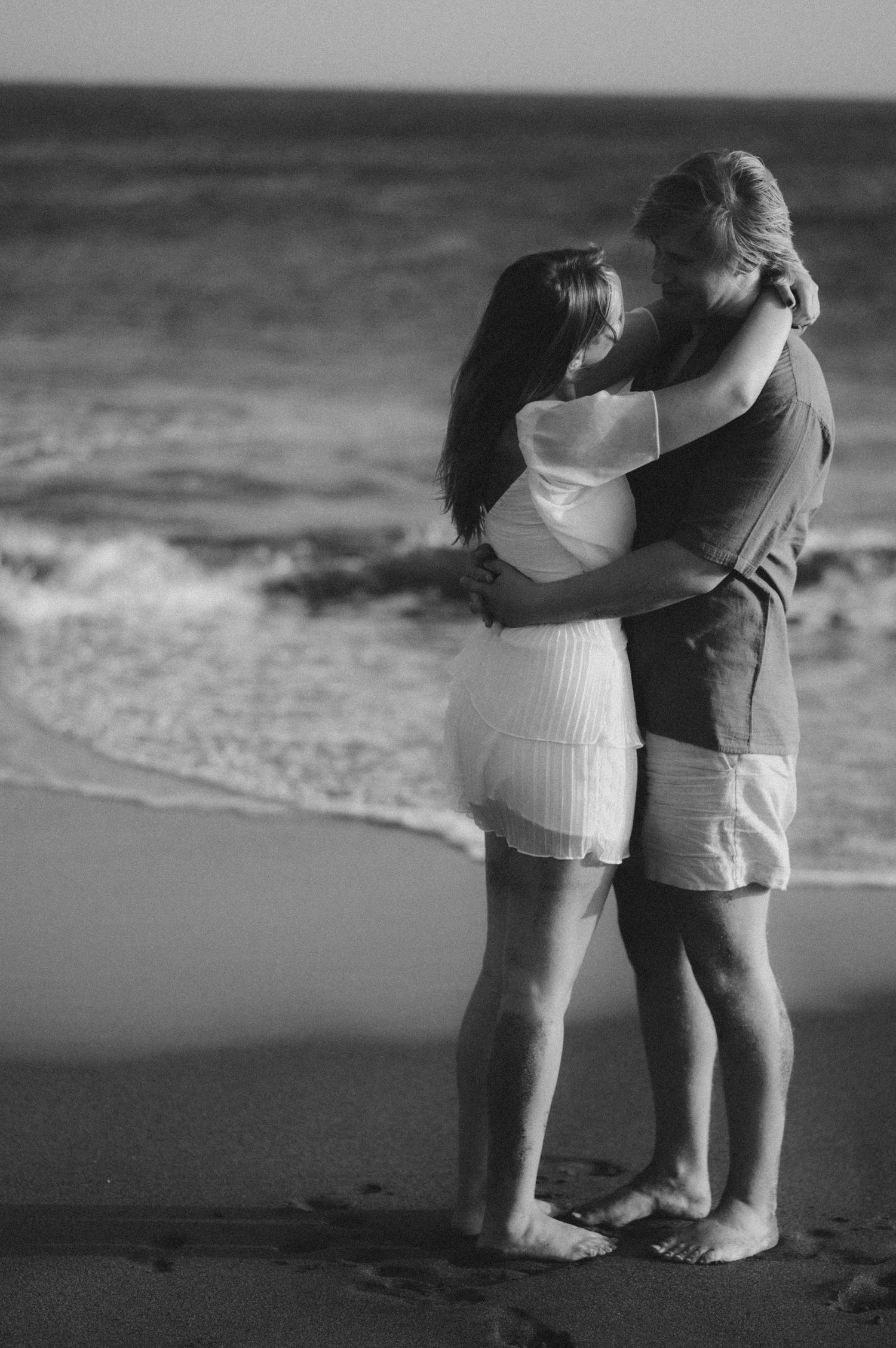 Young loving couple standing close facing each other, expressing their love, barefoot in the sand with ocean in the background at Playa Teji