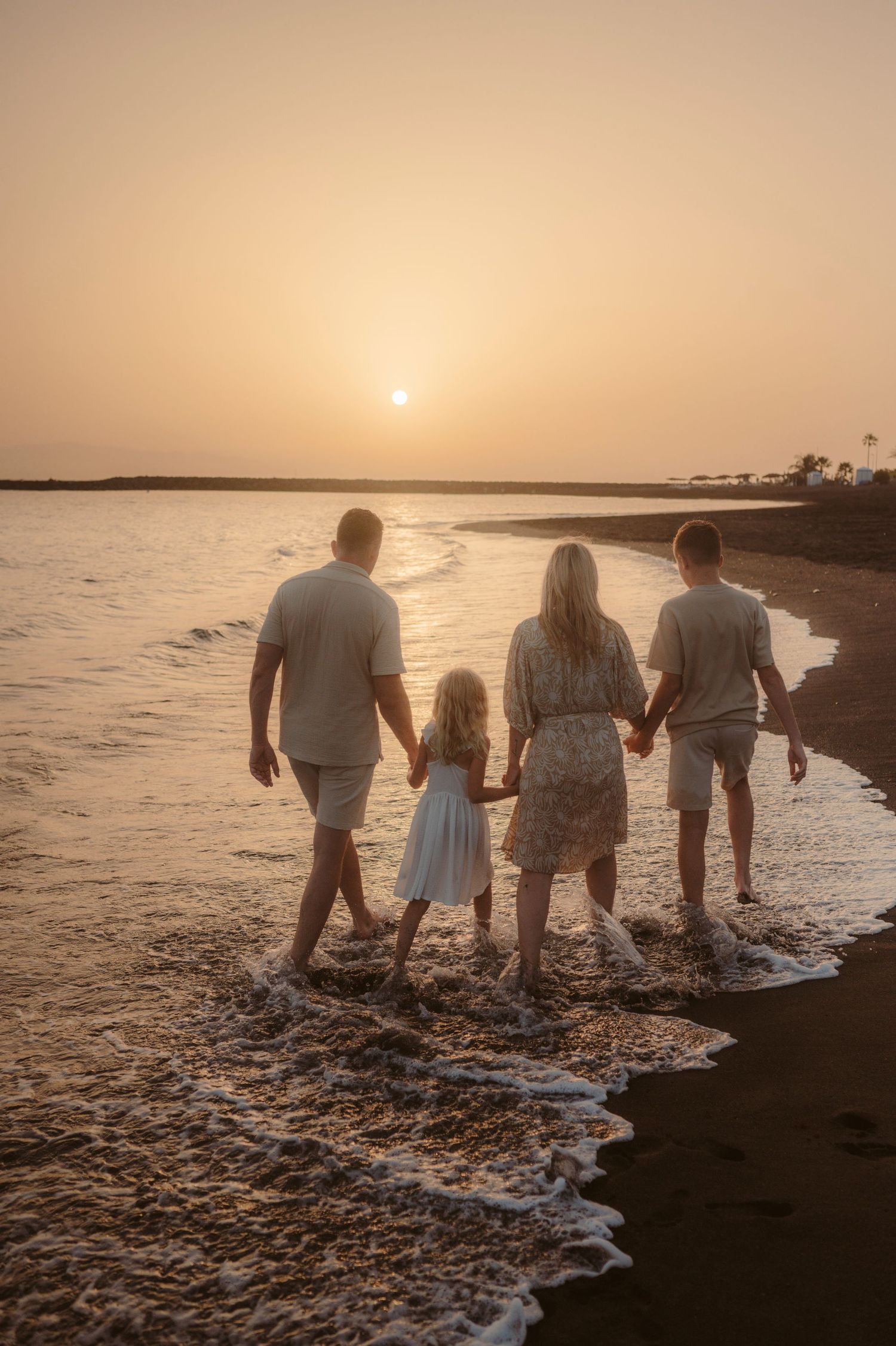 First steps of family into waves on volcanic beach with sunset colors, Tenerife