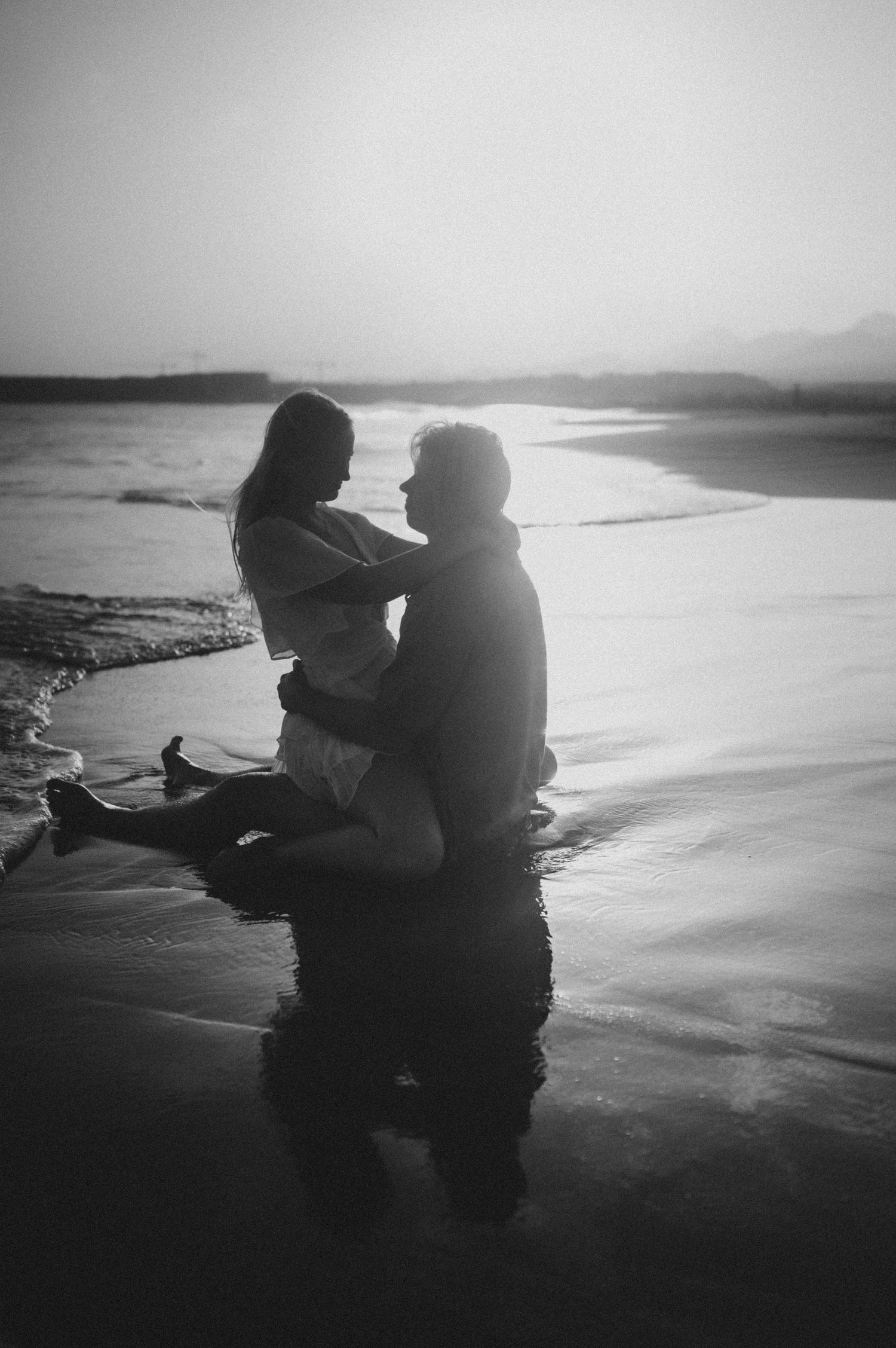 Couple cuddling in the ocean at Playa Tejita during sunset, waves visible in the background, Tenerife couples photoshoot