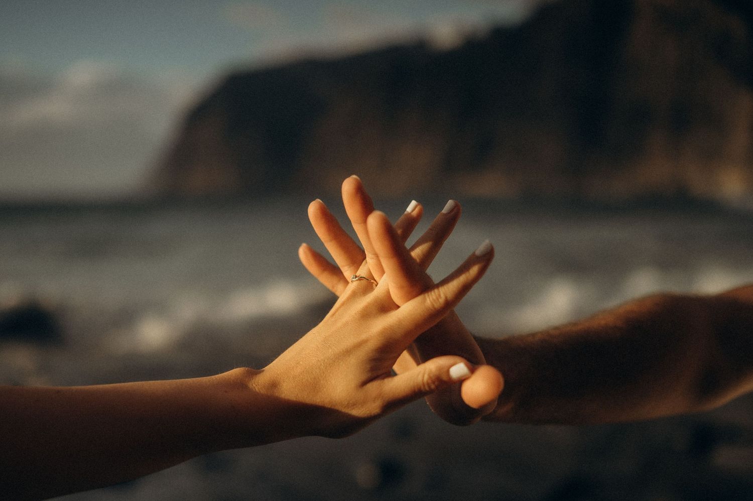 Close-up of couple’s joined hands on Playa de Los Guíos with Los Gigantes cliffs, Tenerife