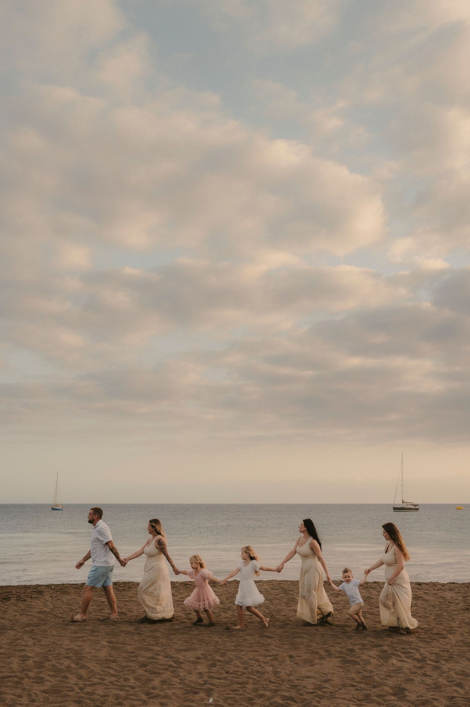Tenerife family photoshoot: large family holding hands in a line on the beach with sea in background