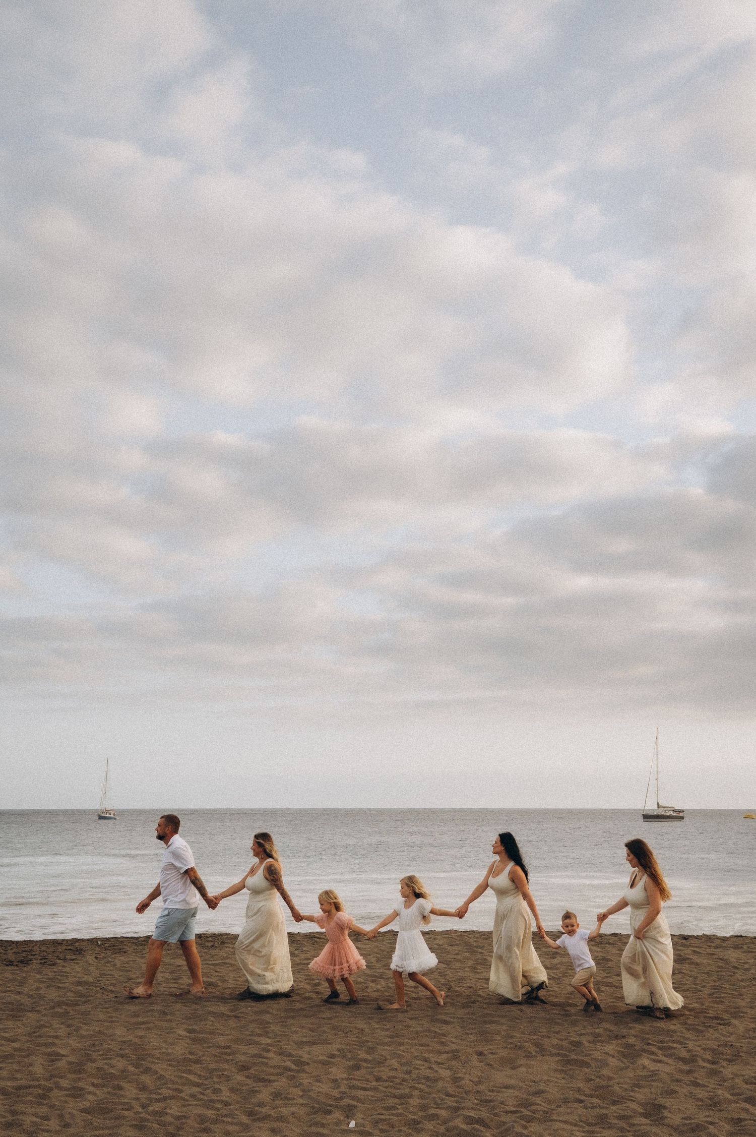 Seven family members holding hands walking along beach by ocean, Playa La Tejita Tenerife
