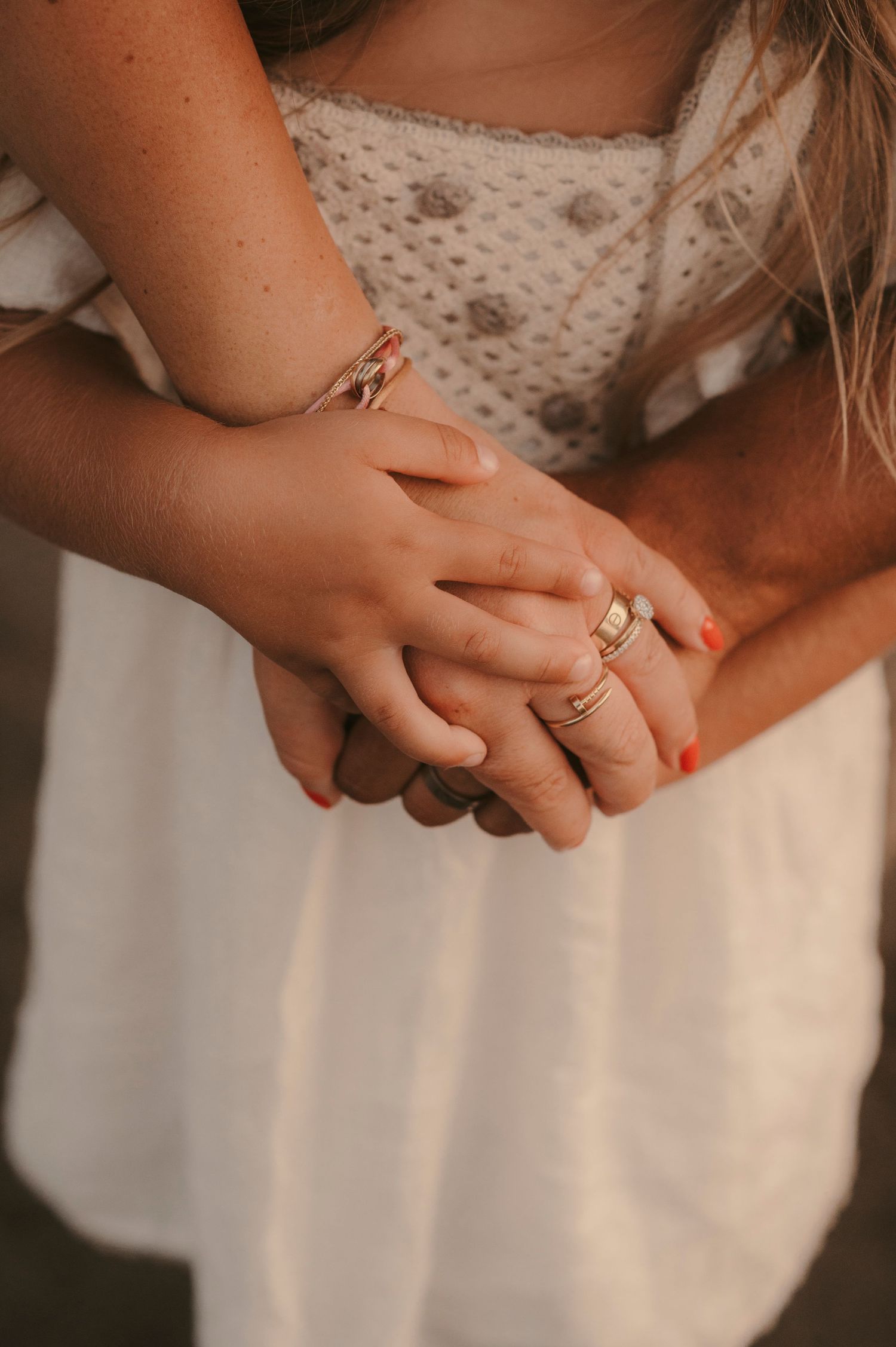 Close up of family hands gently joined in front of their daughter at Playa La Tejita