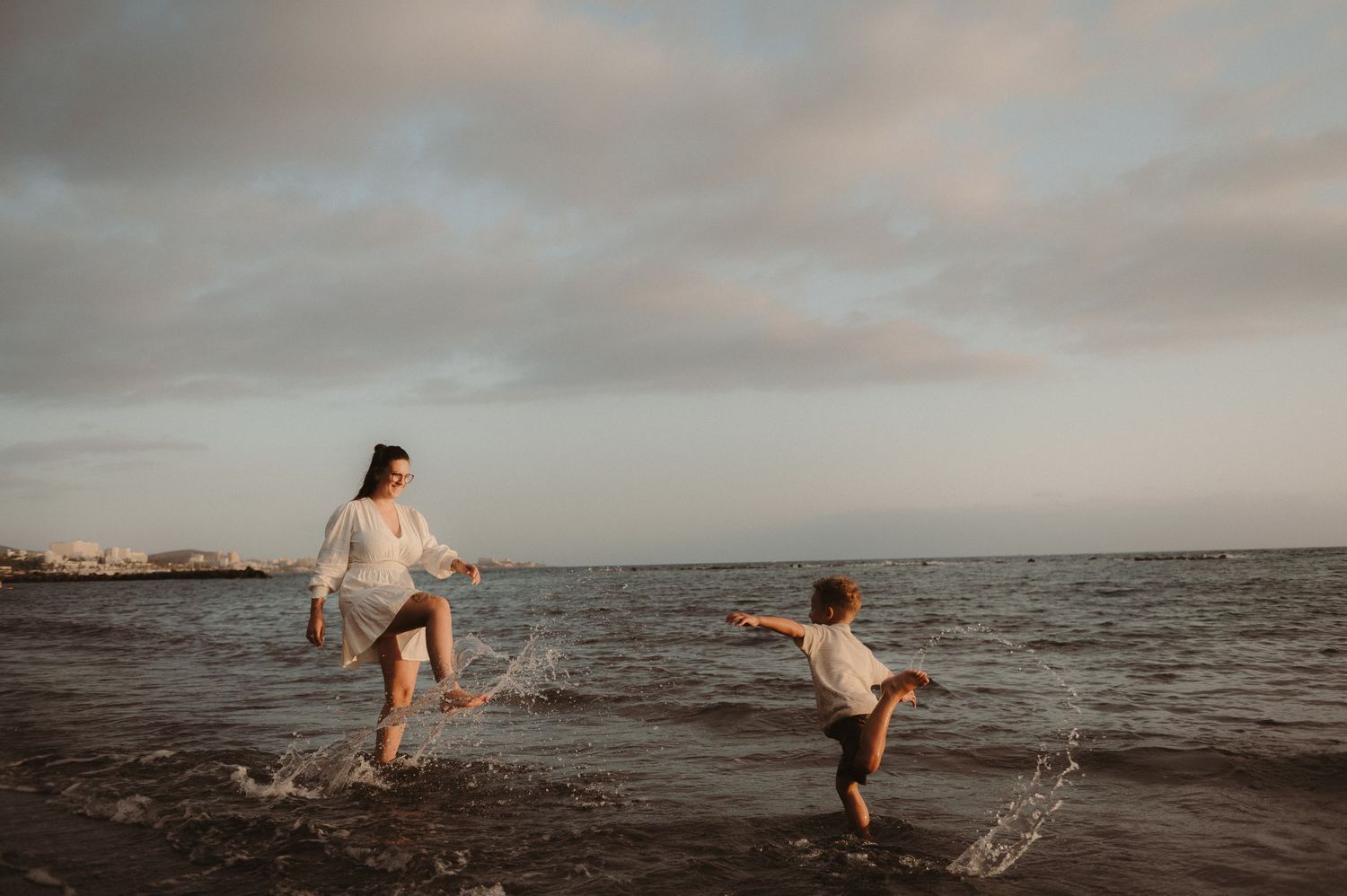 Mother and son standing on beach splashing ocean water at each other with Las Americas behind