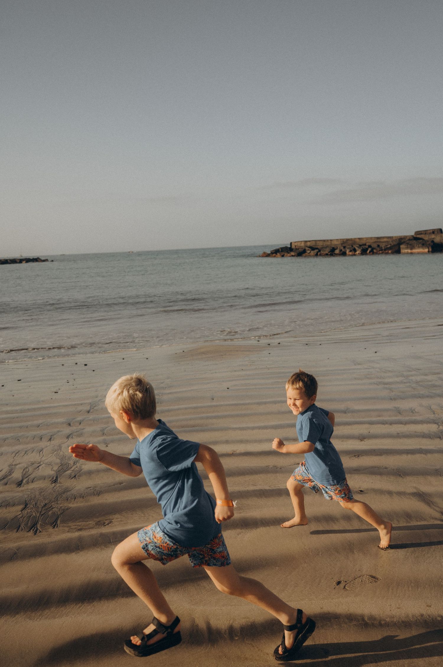 Joyful moment of brothers playing and running along the beach in soft Tenerife morning light at Playa Fañabé