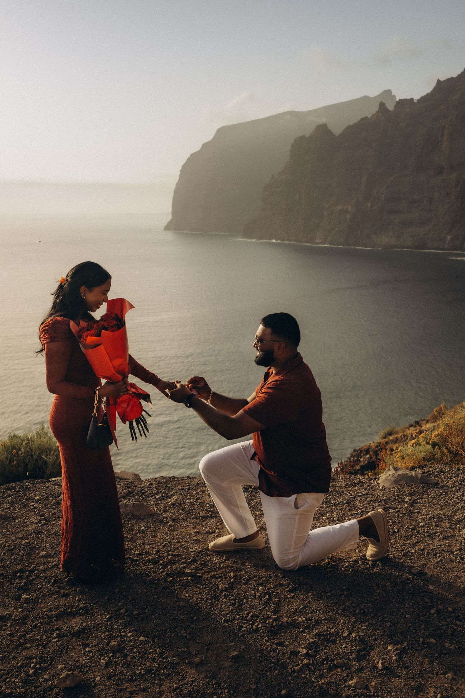 Surprise proposal in Los Gigantes, Tenerife with a romantic couple on dramatic coastal cliffs and ocean backdrop at sunset.
