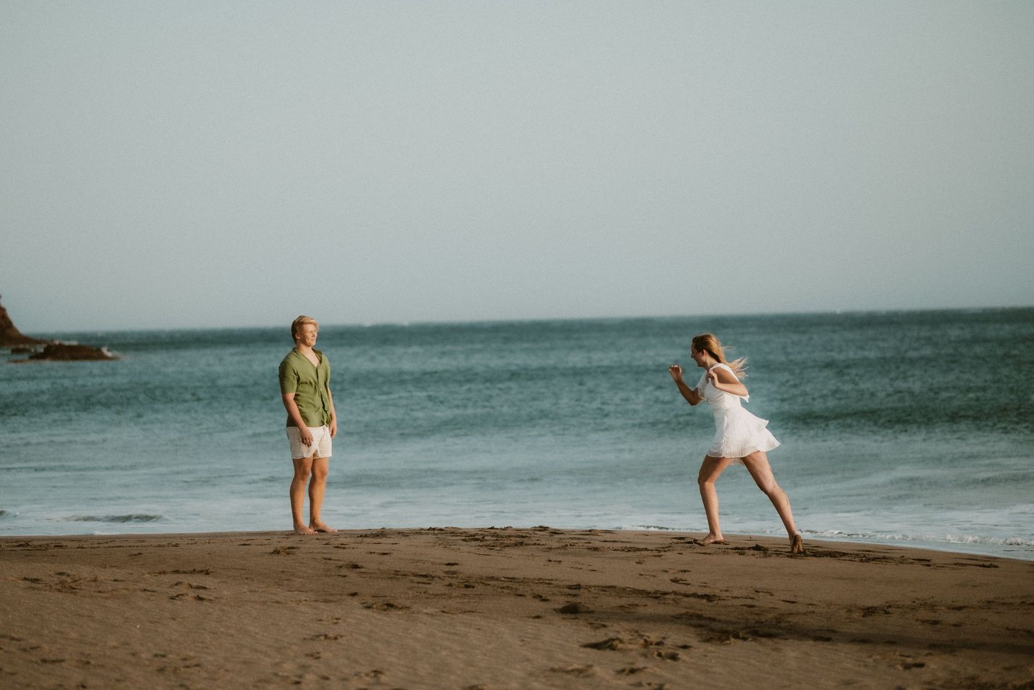 Woman running into her partner’s arms on Playa Tejita with ocean and Montaña Roja in the background, Tenerife couples photoshoot