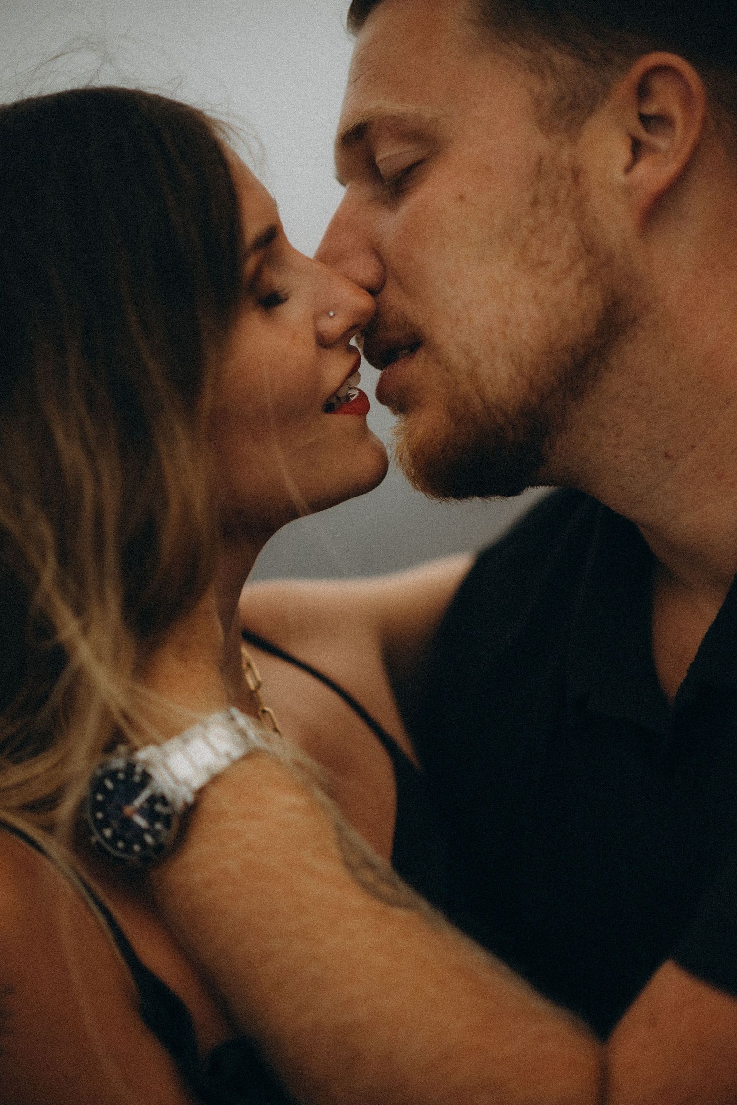 A romantic couple sharing an intimate kiss, the woman wearing a silver watch and the man in a black shirt.