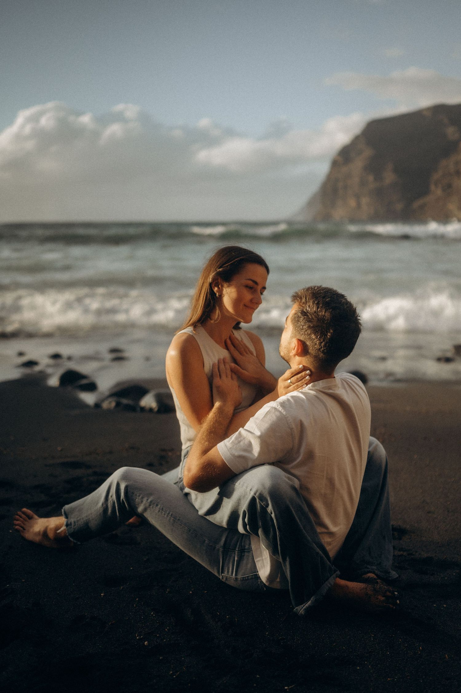 Romantic couple enjoying intimate eye contact on Playa de Los Guíos beach, Tenerife cliffs