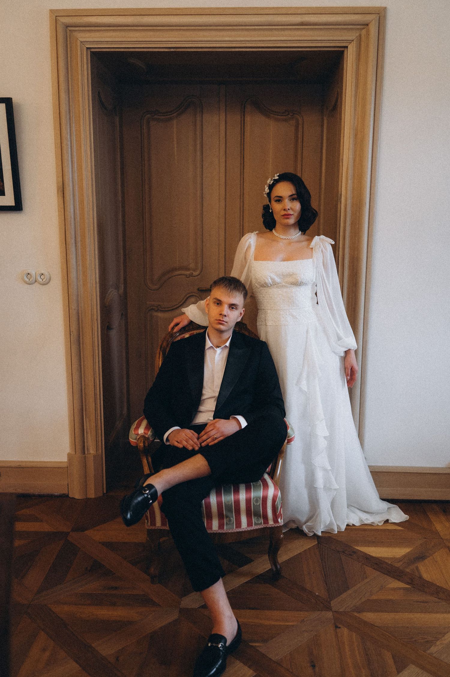Romantic couple portrait with the groom crouching and the bride standing behind him in an elegant pose.