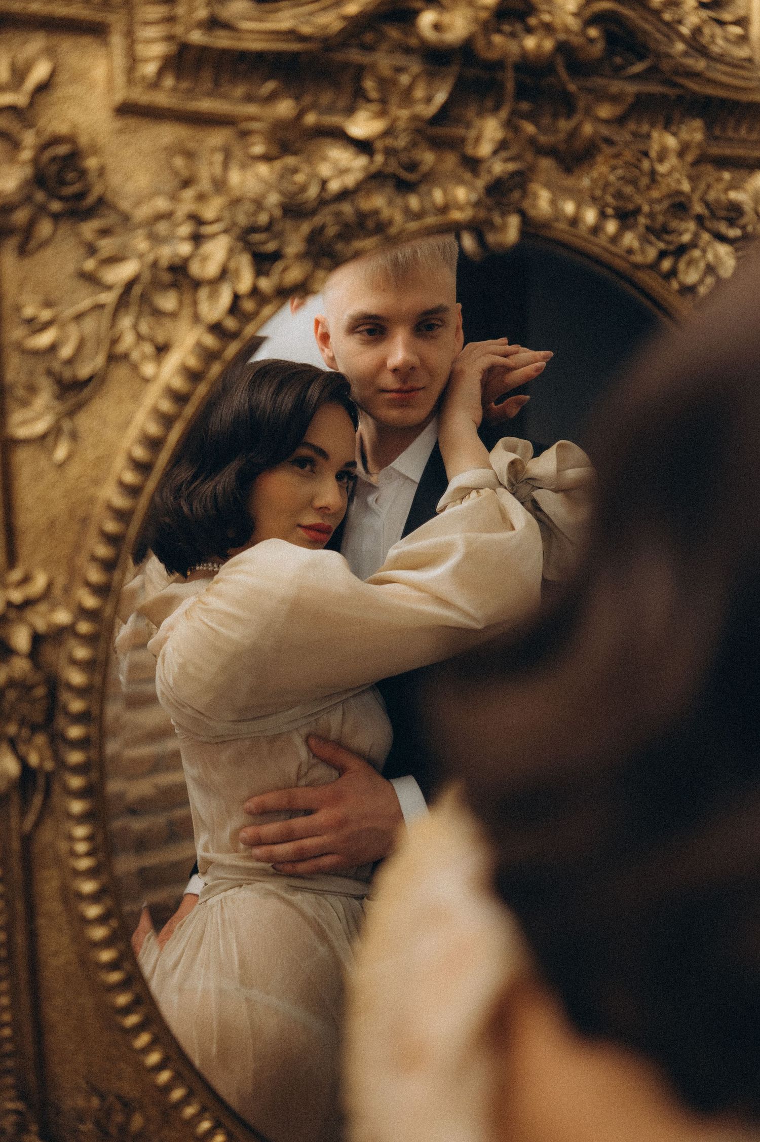 Romantic couple portrait showing the bride and groom embracing, reflected in a mirror while looking into the camera.