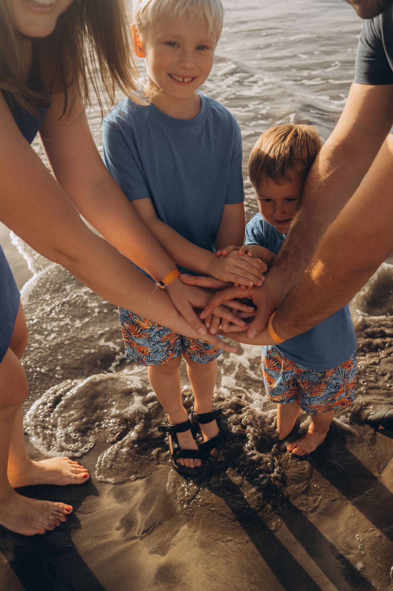 Intimate detail of parents and two boys holding hands in unity with ocean around them at Playa Fañabé