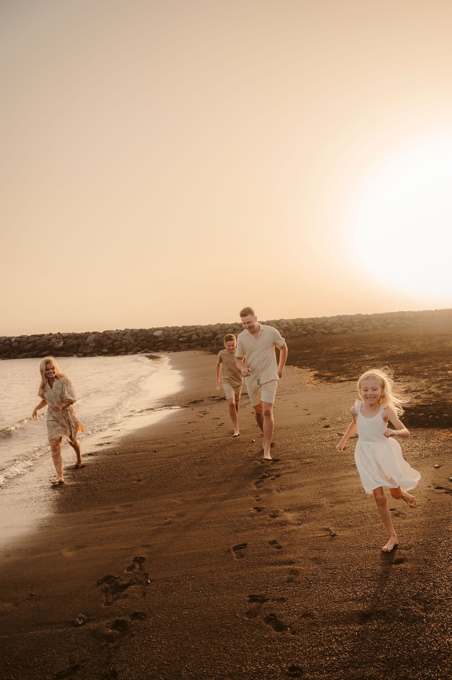 Parents and children enjoying playful run as small waves reach shore, sunset, Tenerife