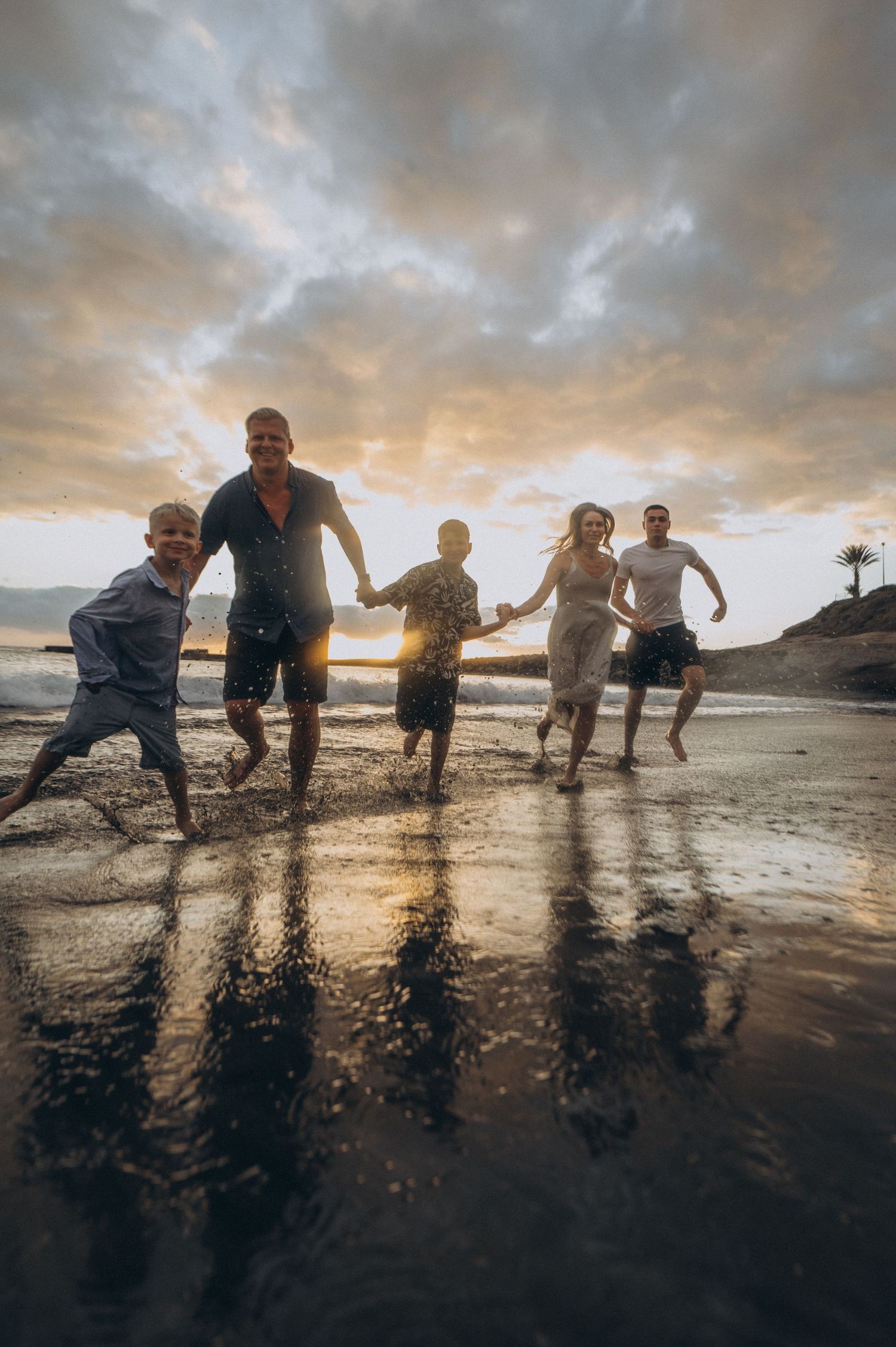 Family together on beach by ocean at sunset with reflections in sand, Playa Fañabé