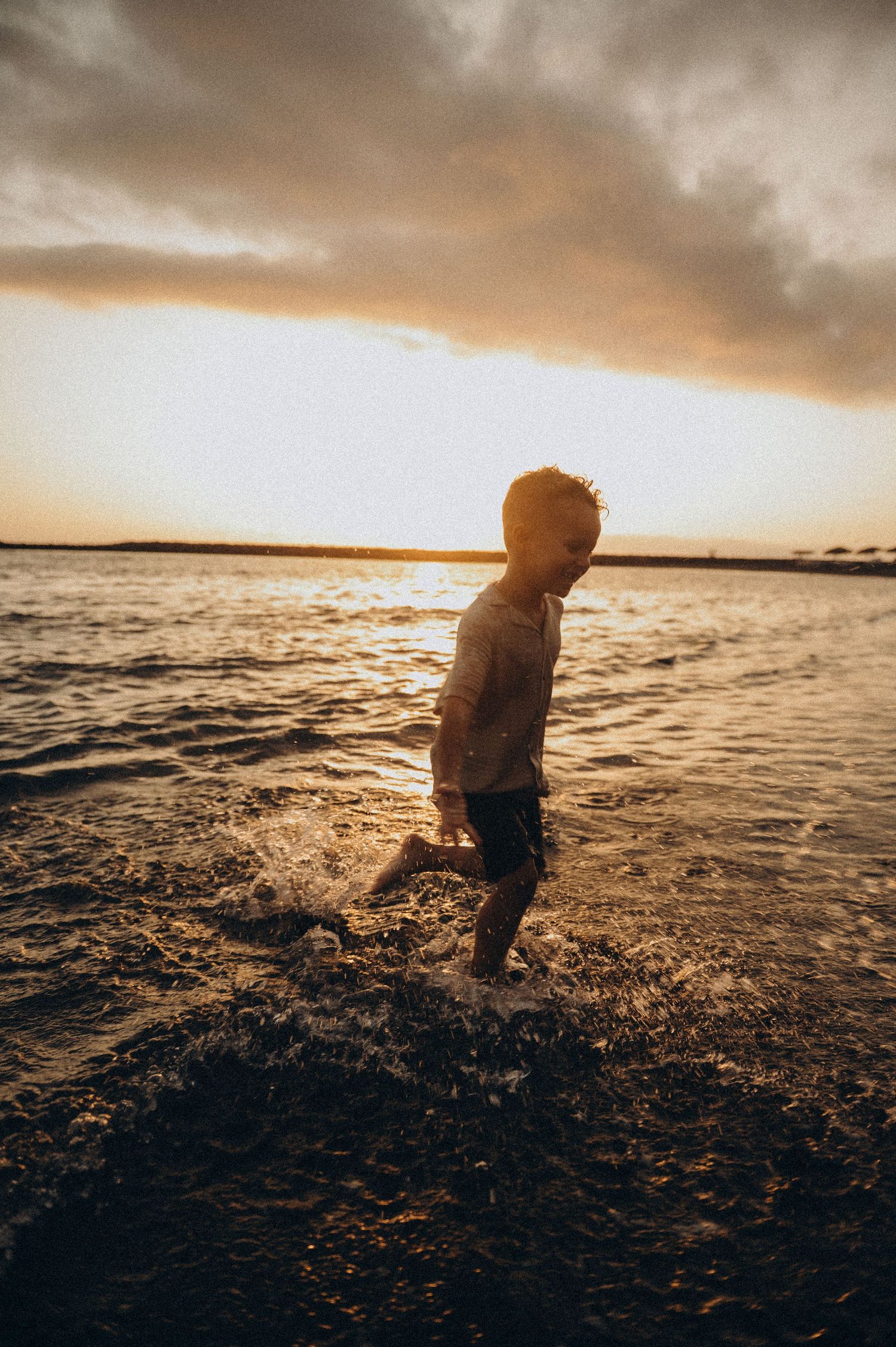 Young boy walking out of ocean at sunset on black sand beach, Playa del Duque