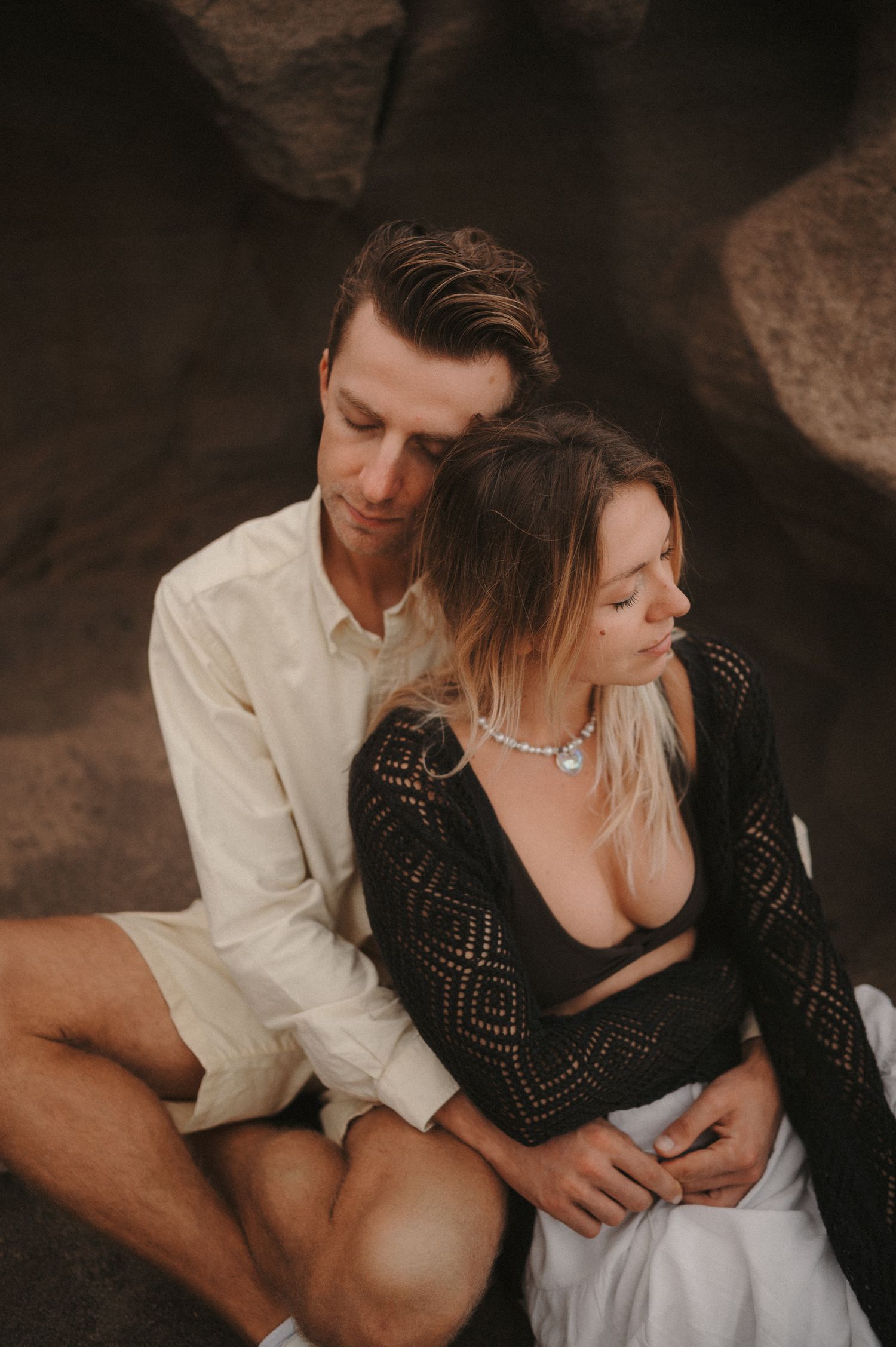 Close-up of a young couple from a different angle, sitting on a cliff with ocean view, enjoying a romantic photoshoot in Tenerife