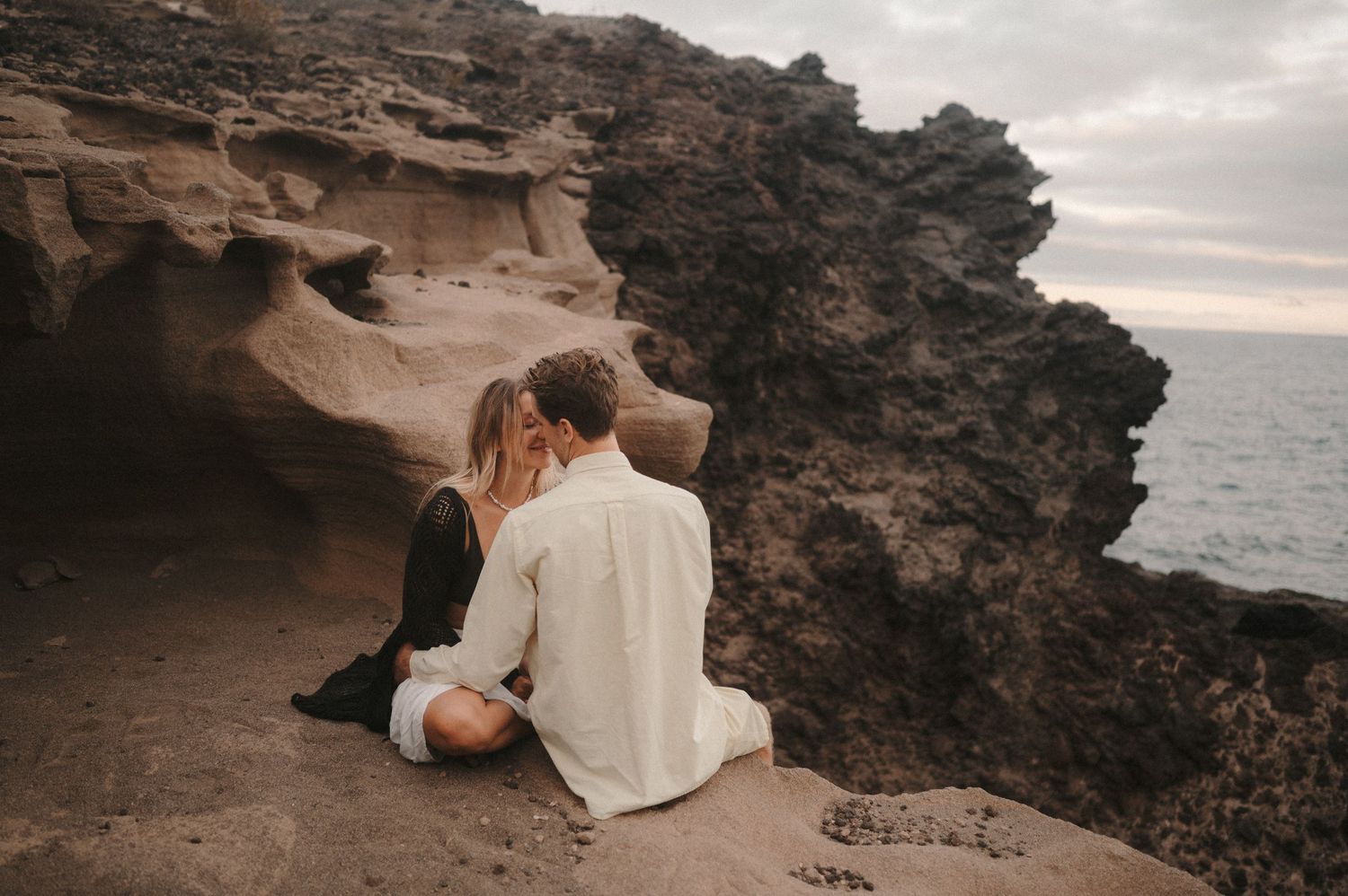 Romantic couple enjoying a photoshoot at the colorful cliffs near Montaña Roja with ocean in the background, Tenerife