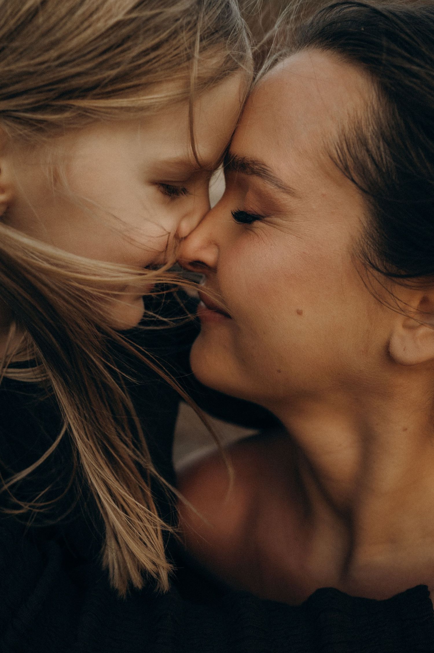 A mother and young daughter share a tender forehead-to-forehead moment, eyes closed, in an intimate close-up portrait. Playa de La Tejita.