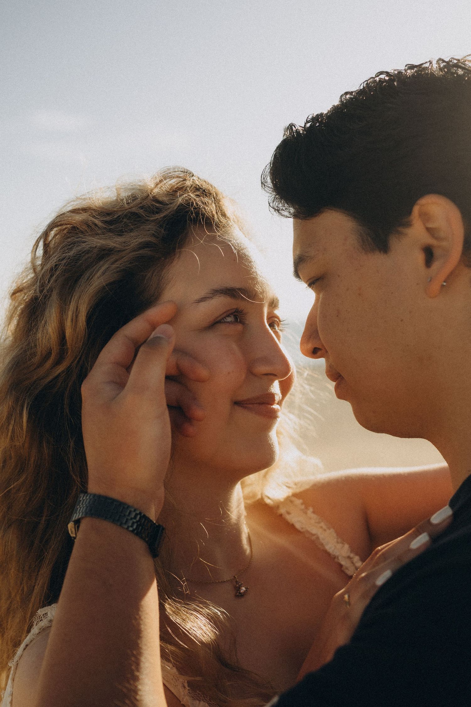 Romantic couple sharing a tender moment outdoors, man gently touching woman's face in golden sunset light.