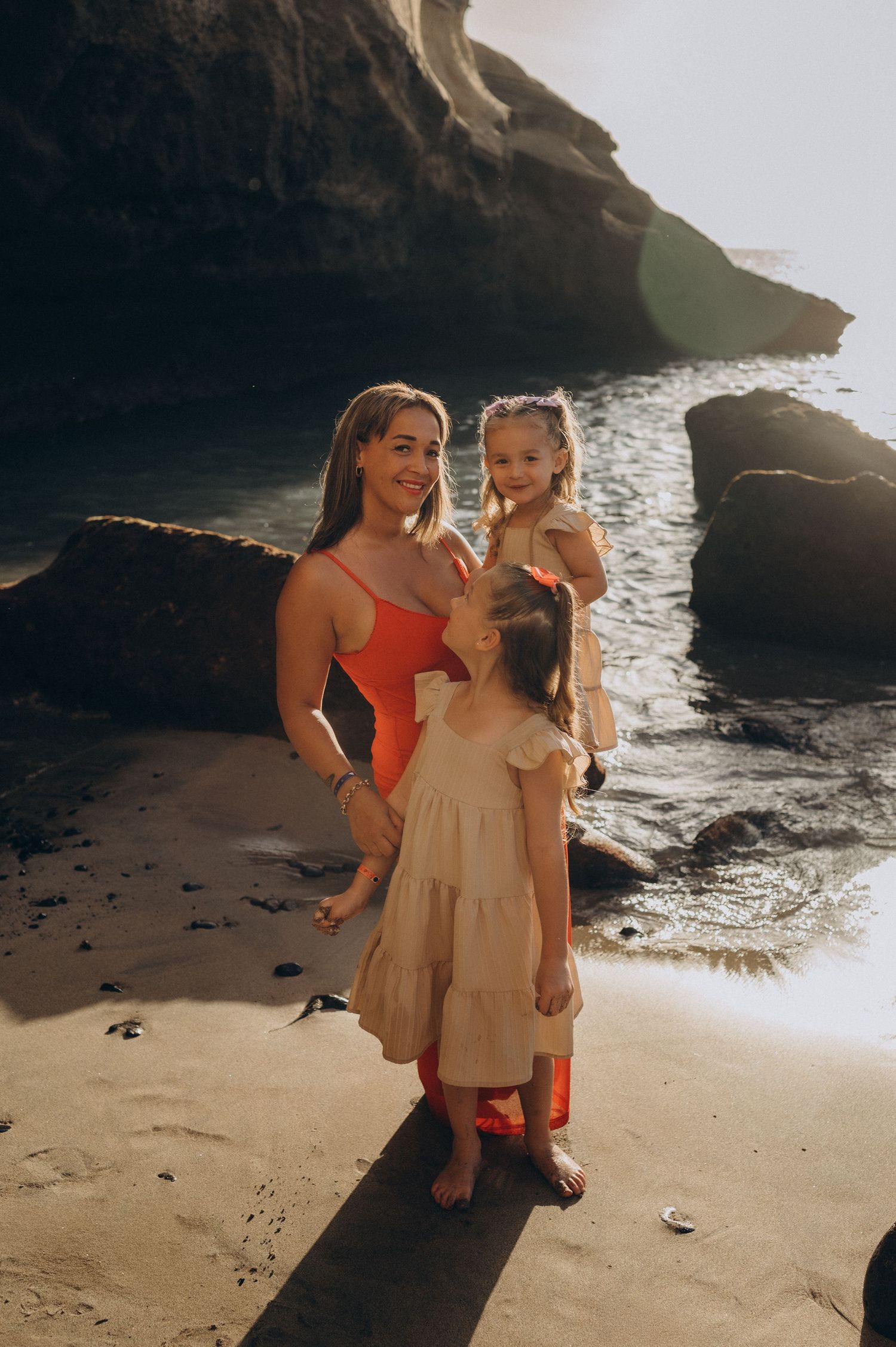 Mother holding her daughter with sunset light and Atlantic waves in the background at Playa Morteros