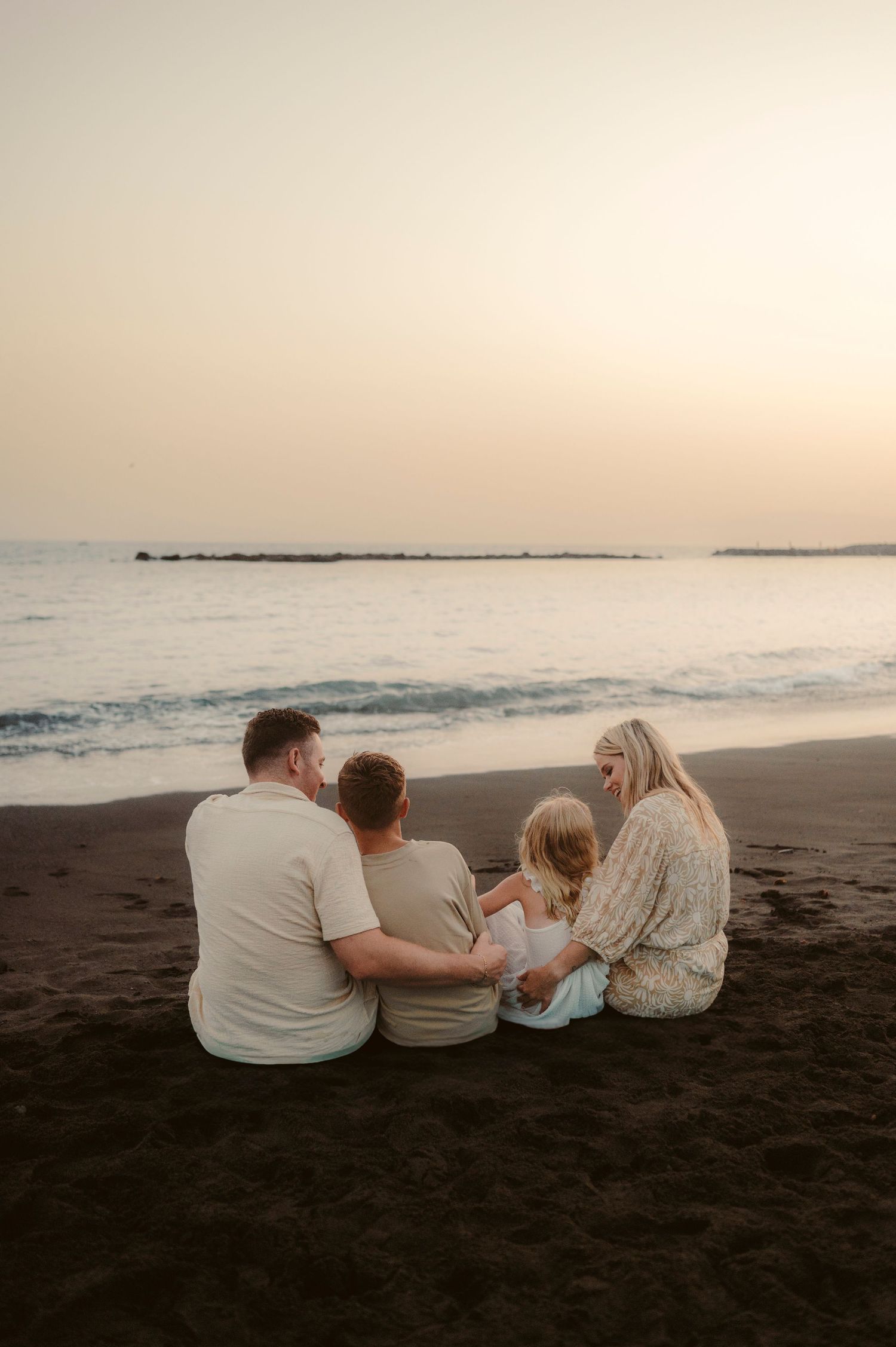 Entire family sitting together in arms enjoying ocean view and sunset, Playa del Duque