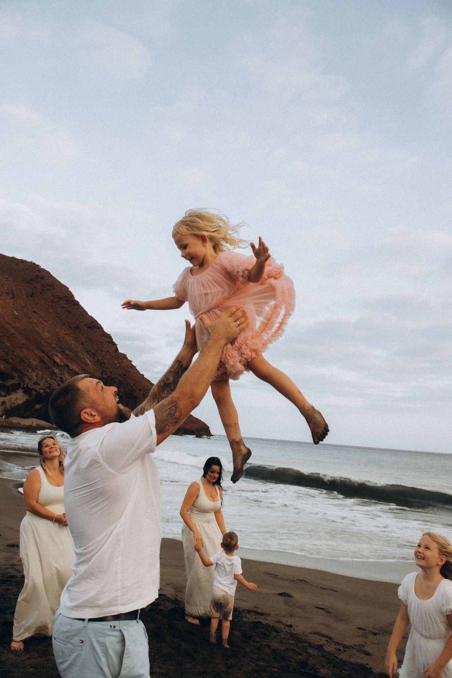 Father tossing 2-year-old daughter in the air on beach, Playa La Tejita Tenerife