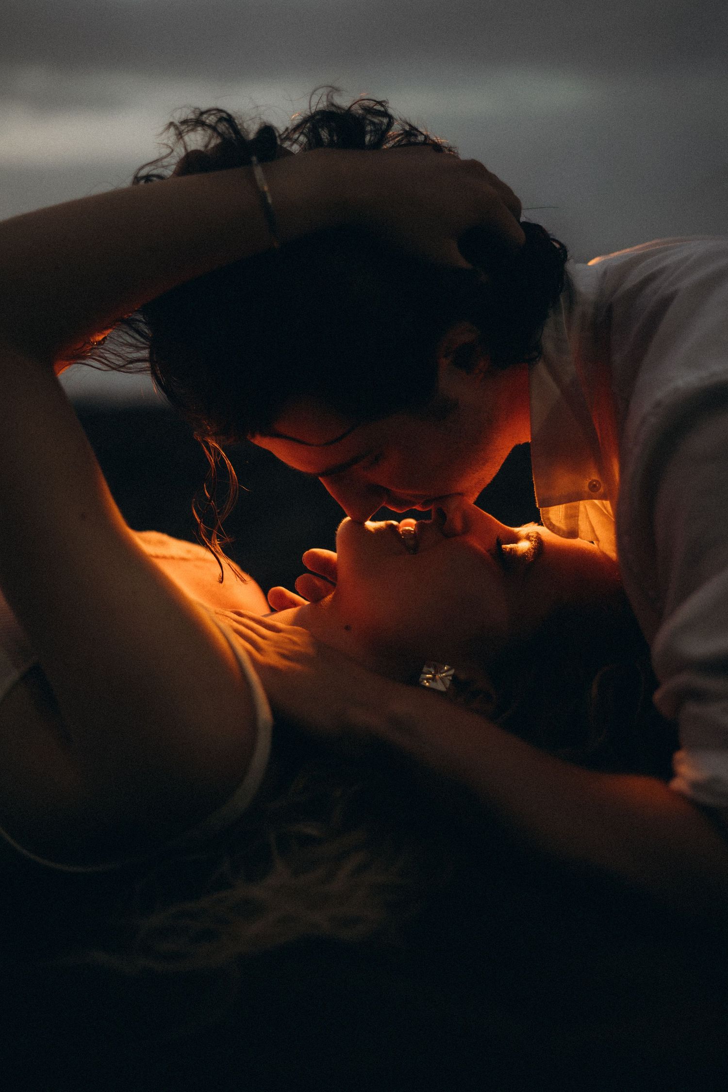 Romantic couple sharing a tender kiss in warm golden light against a dark moody background.