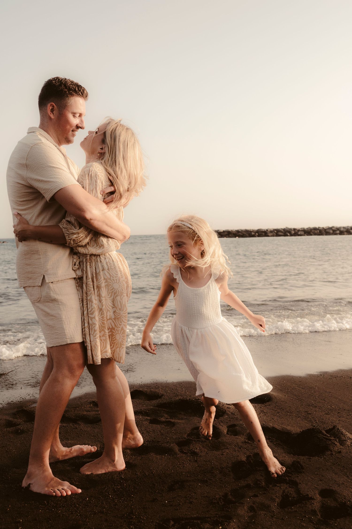 Father holding son in arms while daughter runs by ocean at sunset, Playa del Duque