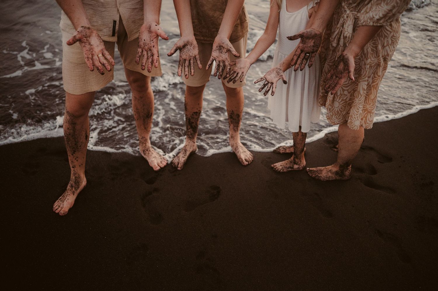 Close up of family hands and feet on black sand with white waves at Playa del Duque, Tenerife