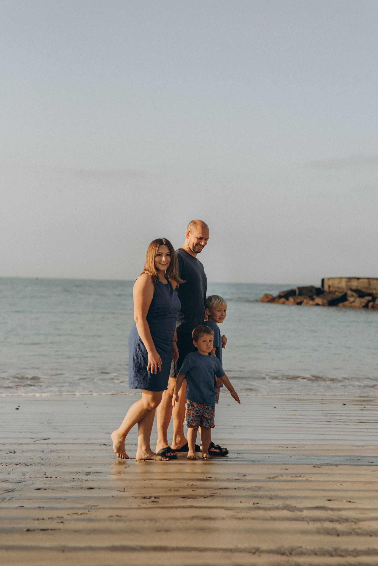 Tender family moment of four walking hand in hand on the shore captured from afar at Playa Fañabé, natural family photography