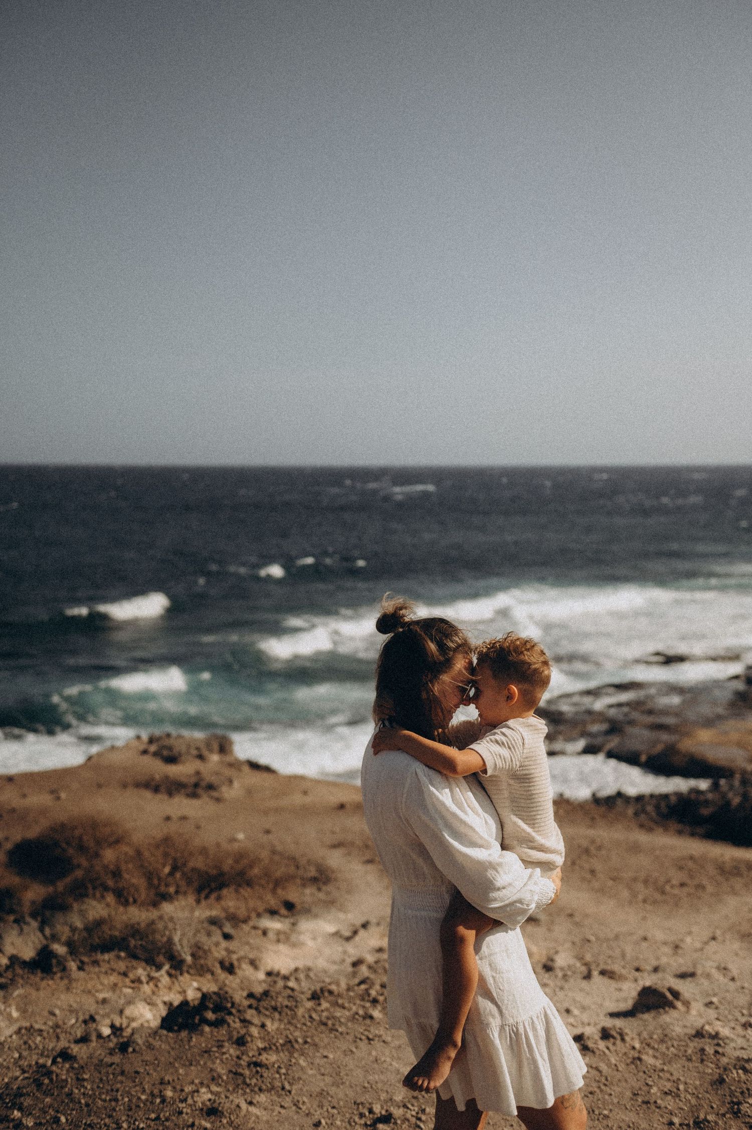 Intimate moment with mom and young son in embrace near ocean, Playa Montaña Pelada Tenerife