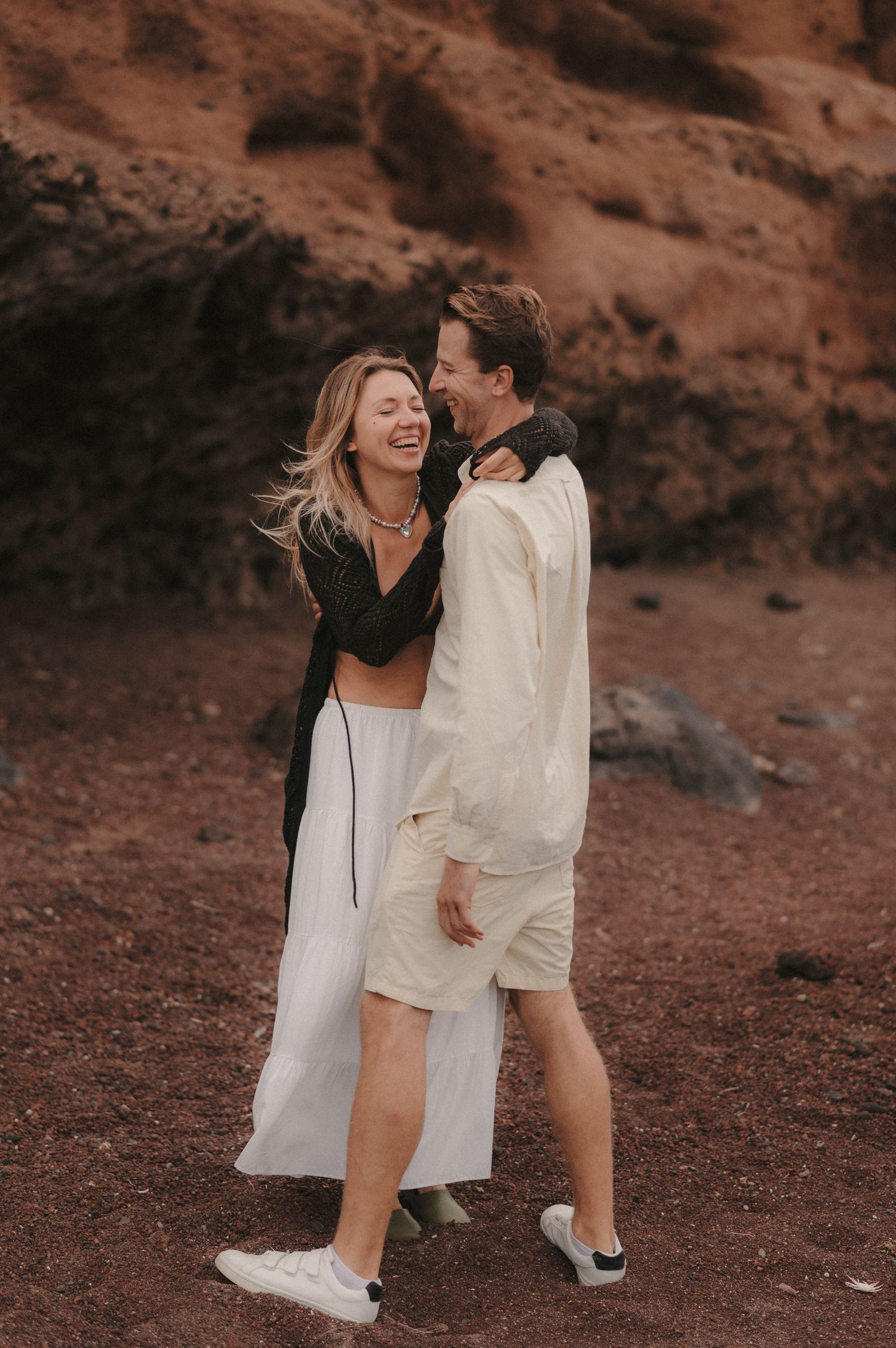 Candid moment of a couple standing together, she smiling beautifully with cliffs and rocks under Montaña Roja in the background, Tenerife