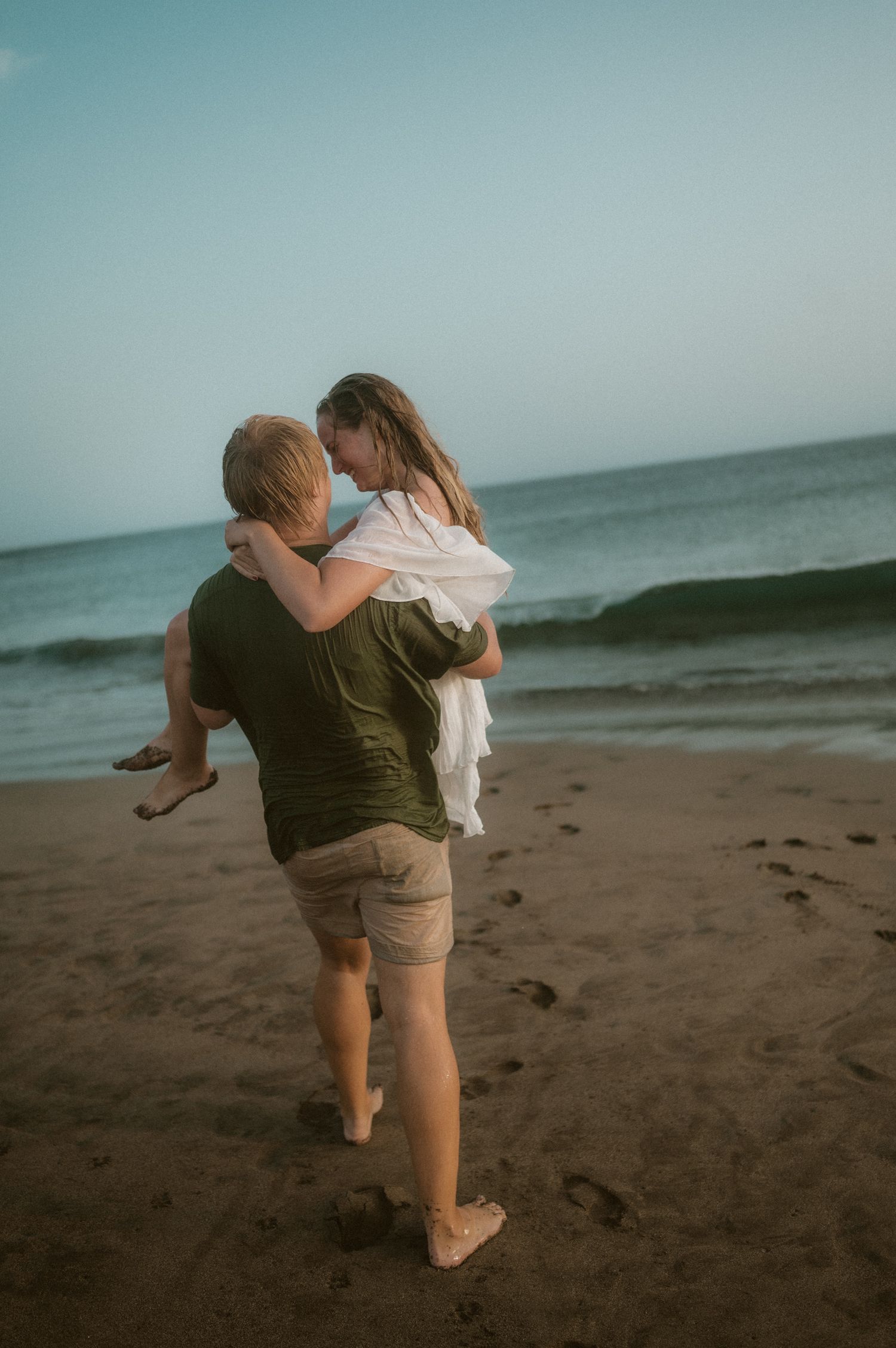 Man holding his partner above the sand at Playa Tejita with ocean and Montaña Roja in view